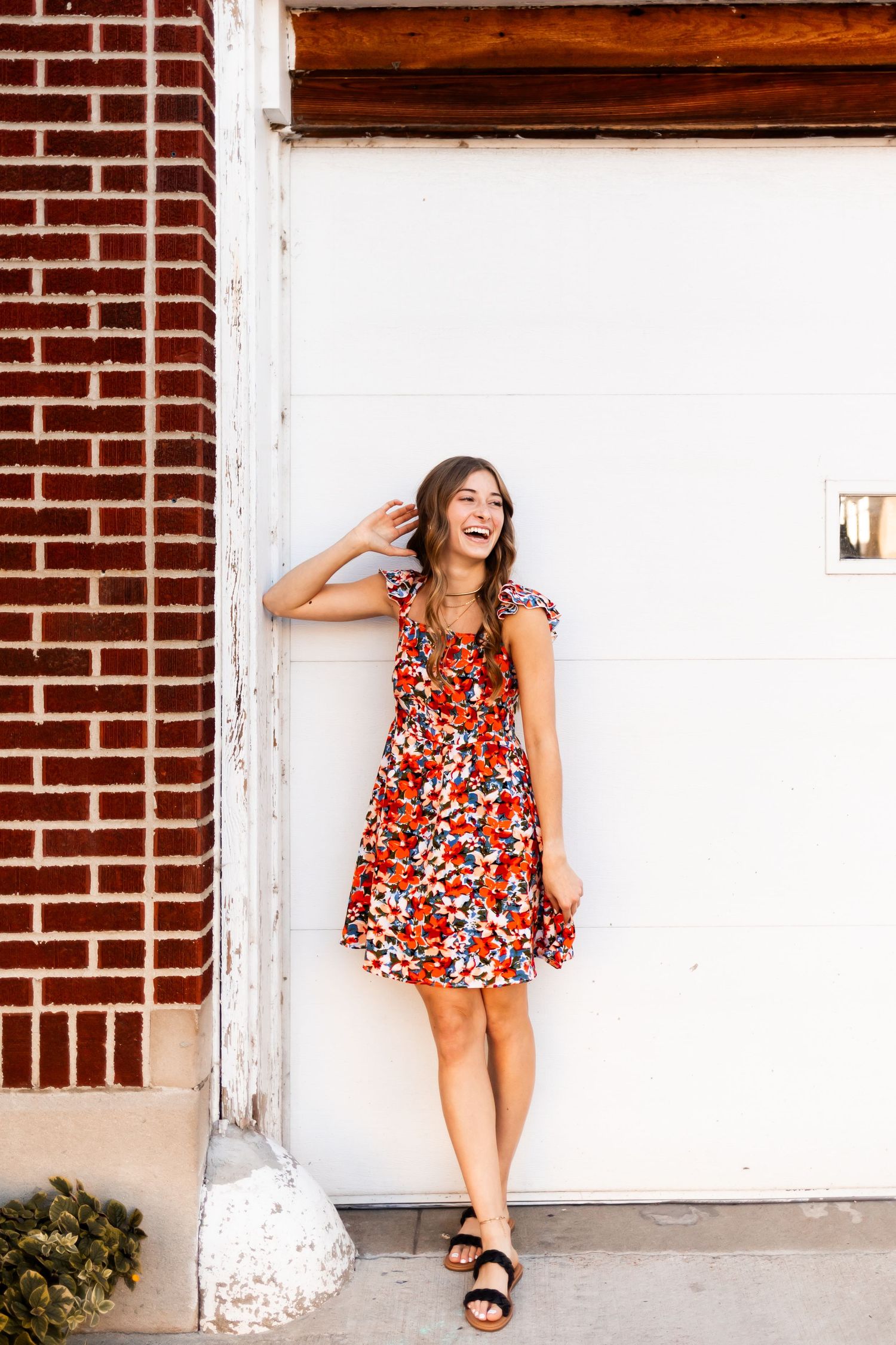 Summer portrait in floral dress against white and brick wall.