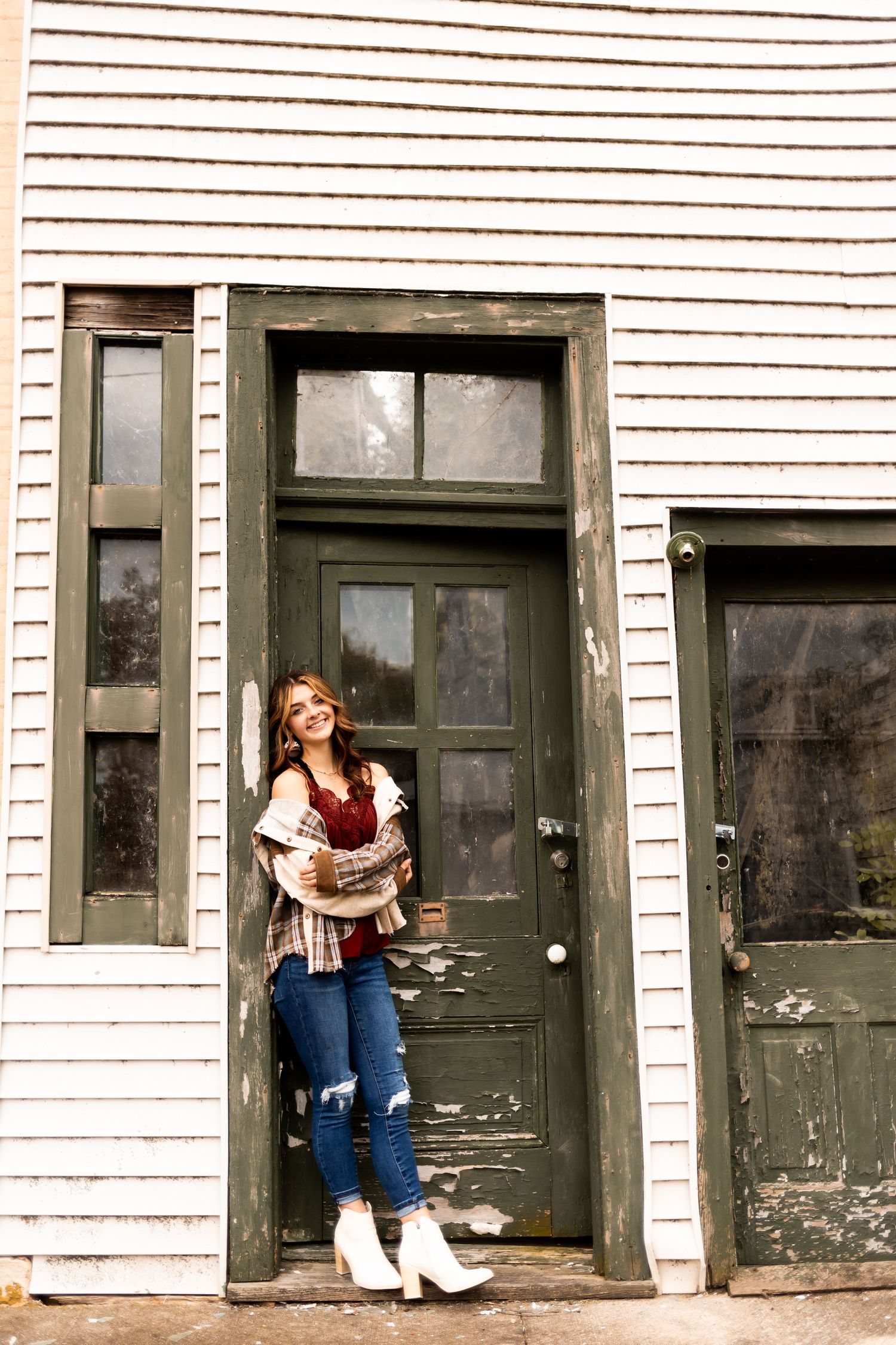 Vintage-style photo by a weathered doorway of a person in white boots and jeans against white siding.