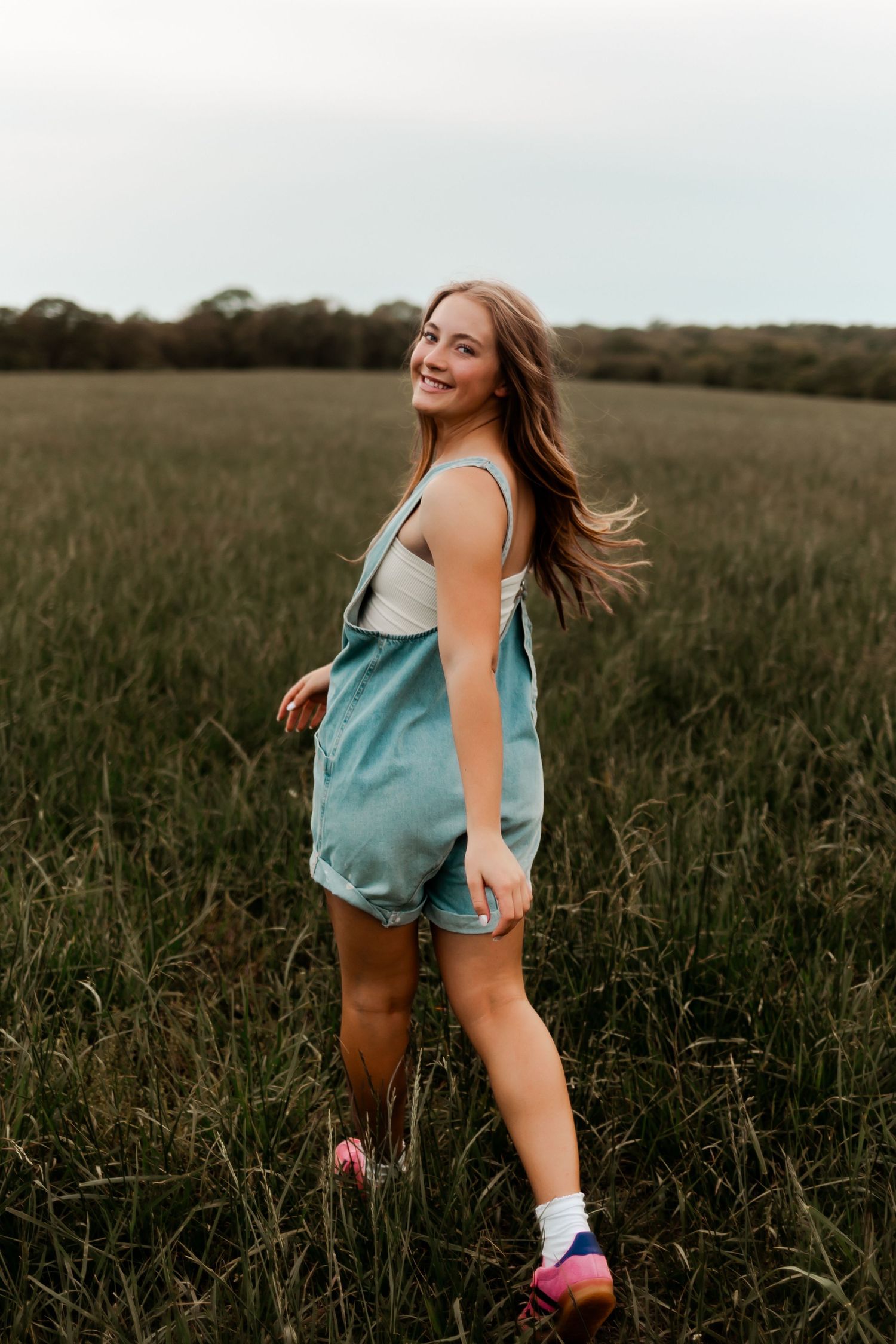 A person twirls in a teal romper in a sunlit meadow.