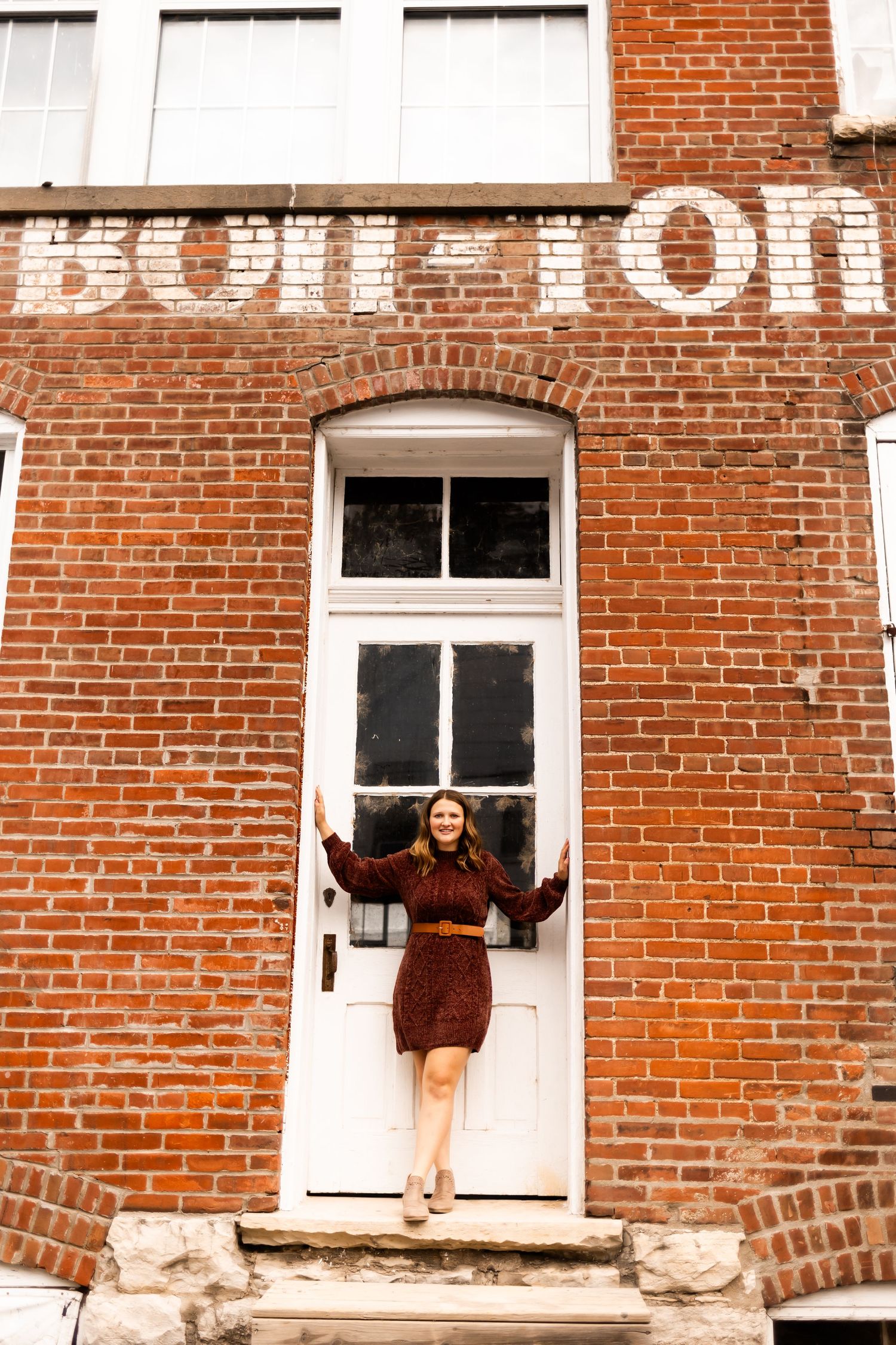 Nostalgic architectural shot with someone posing in a doorway of a rustic brick building with faded text.