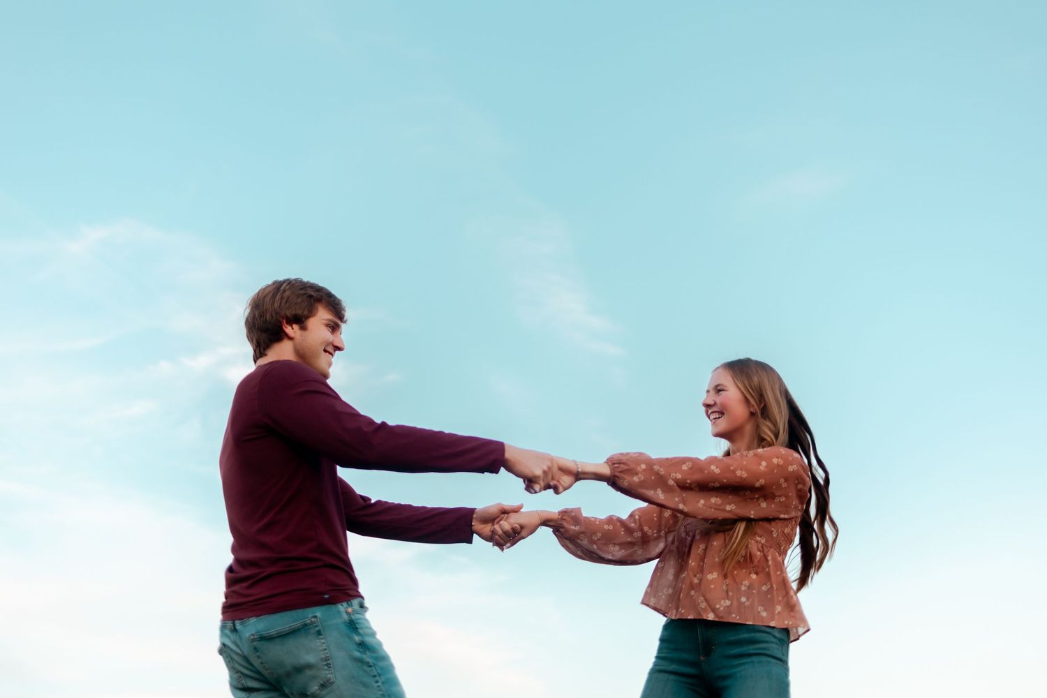 Two people hold hands in a playful pose against a bright blue sky.