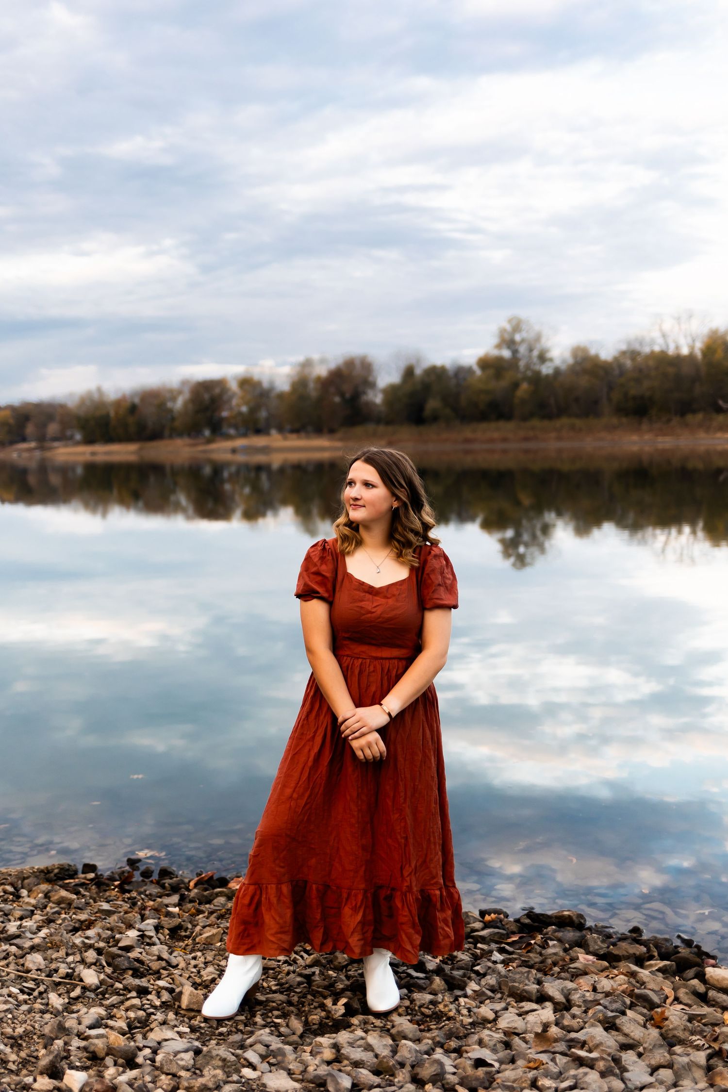 A picturesque lakeside portrait featuring a long red dress and reflection of autumn trees in calm waters.