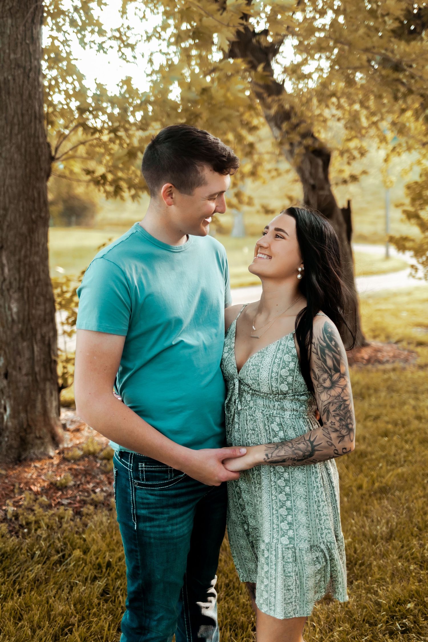 Couple shares tender moment in park setting with golden autumn trees in background.