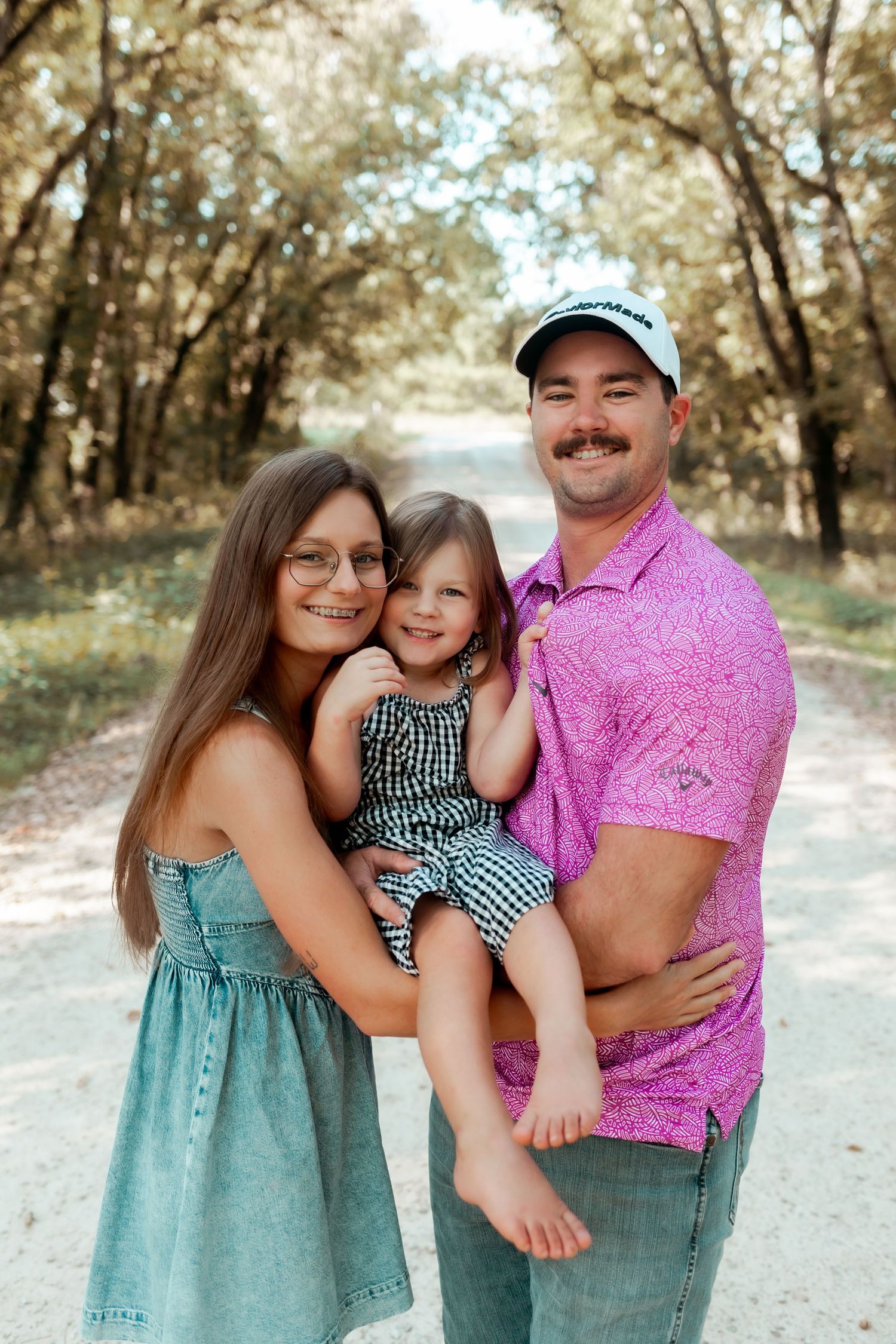 A family in coordinated outfits poses together on a tree-lined path.