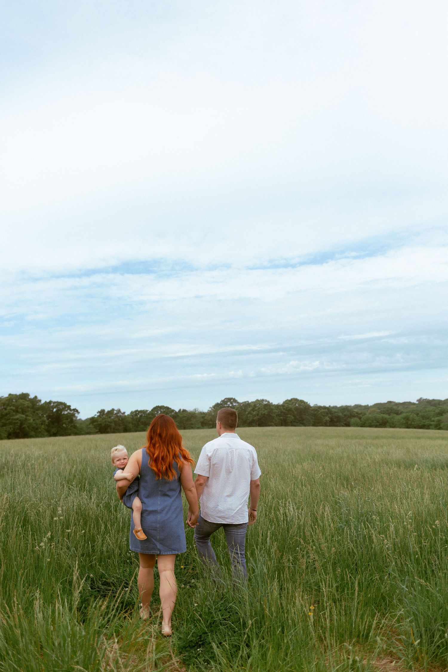 Three people walking through a serene meadow with tall grass and blue sky.
