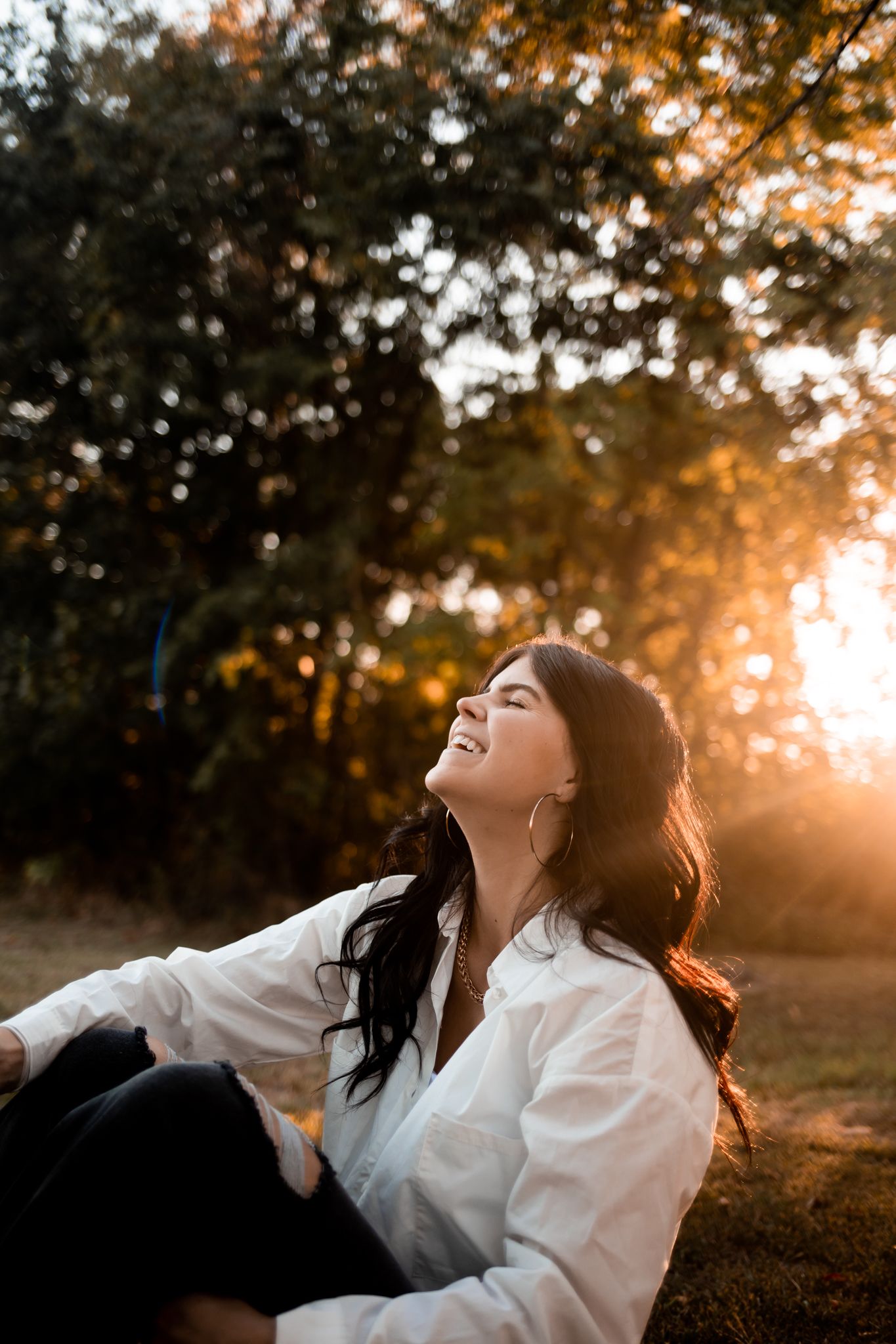 Woman enjoying sunset in white shirt sitting outdoors with golden light.