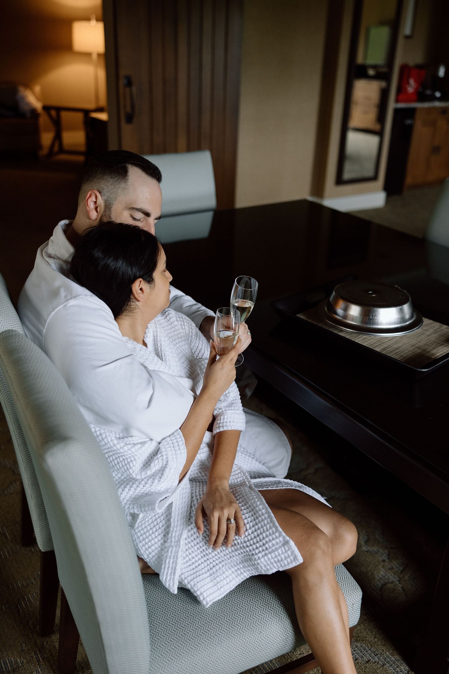 A couple in white bathrobes relaxing with champagne in a luxurious hotel room.
