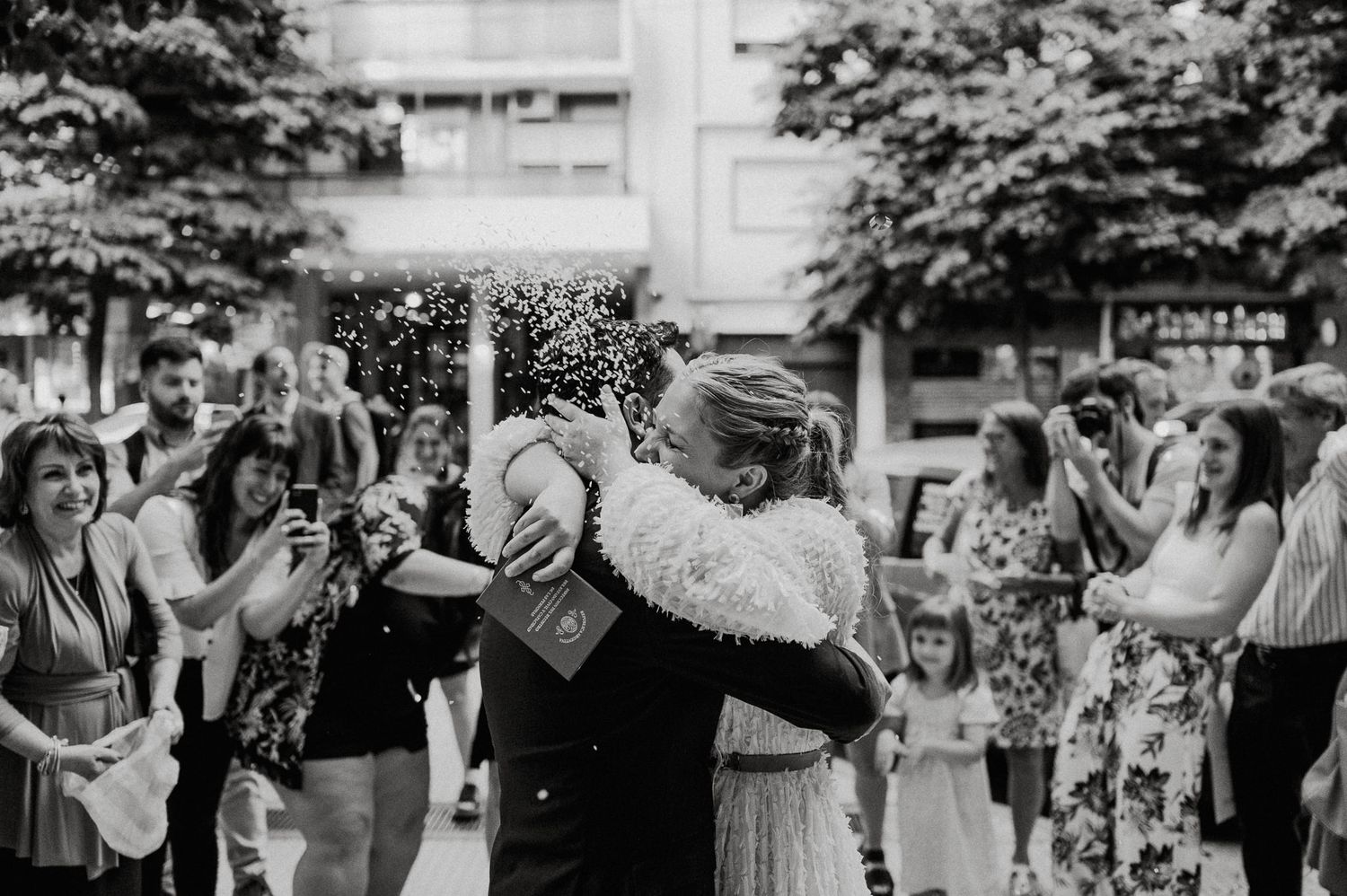 A couple shares a romantic dance outdoors surrounded by guests while glitter confetti falls in a black and white scene.