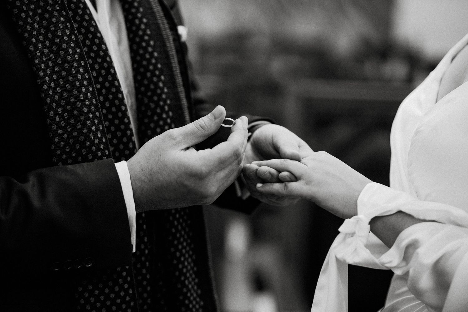 A black and white close-up photo of hands exchanging wedding rings during a marriage ceremony.