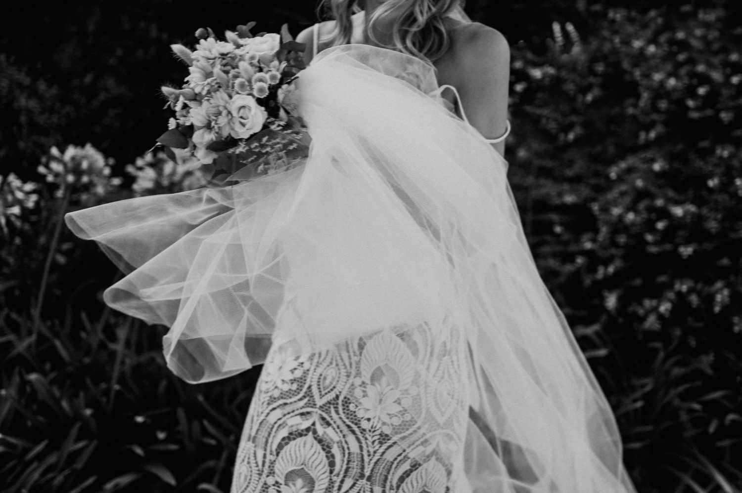 Close-up detail of flowing lace wedding dress and bouquet in motion.