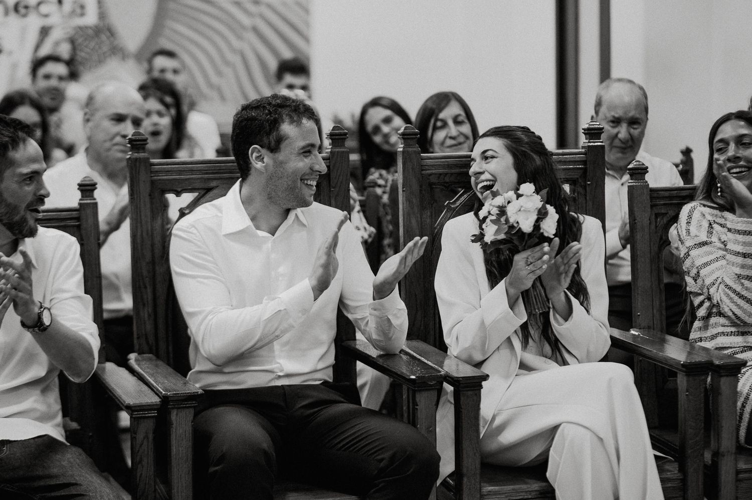 A joyful black and white candid moment showing people laughing together while seated in church pews during a service.