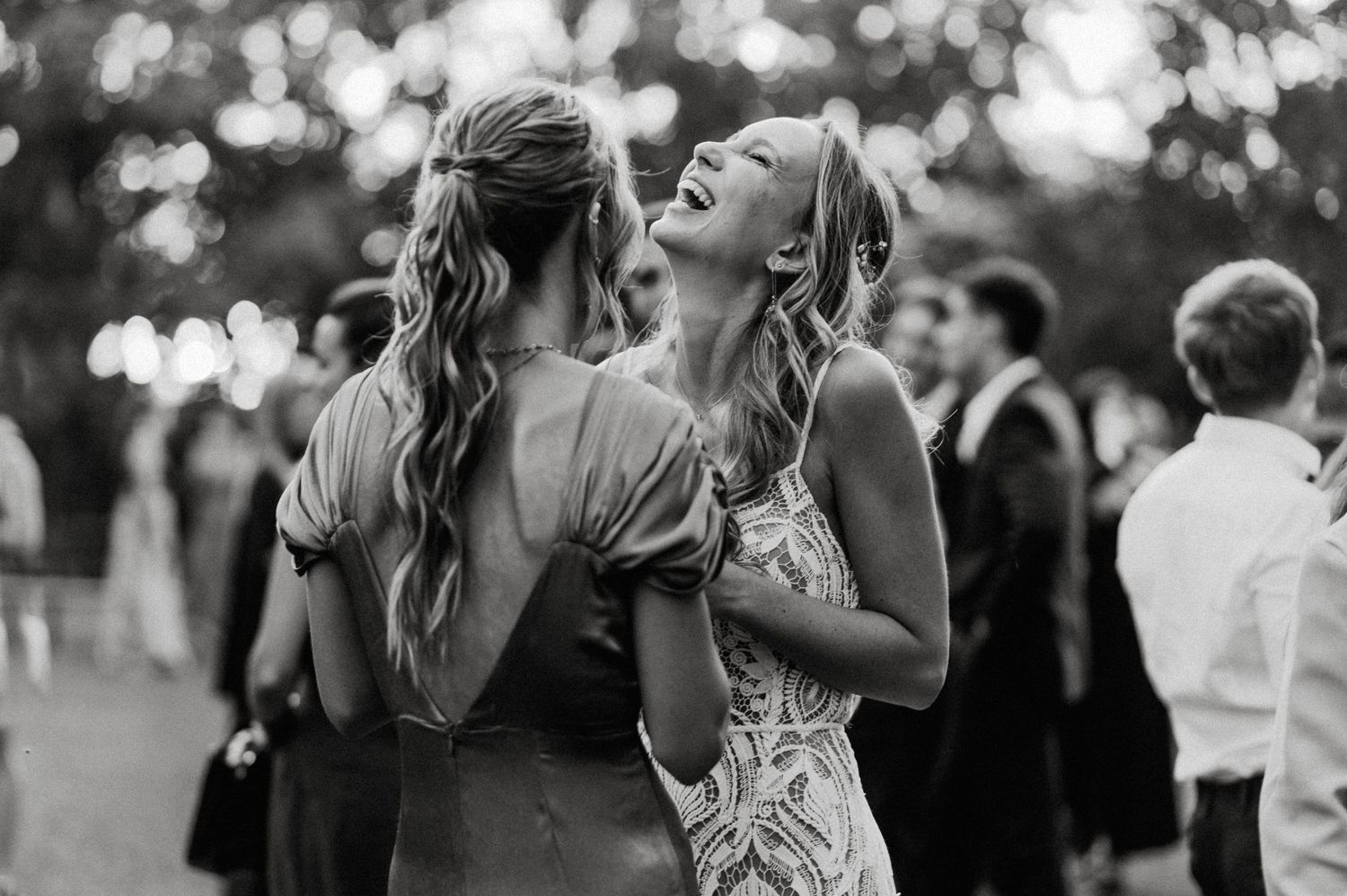 Two wedding guests share a joyful moment on the dance floor at an outdoor reception.