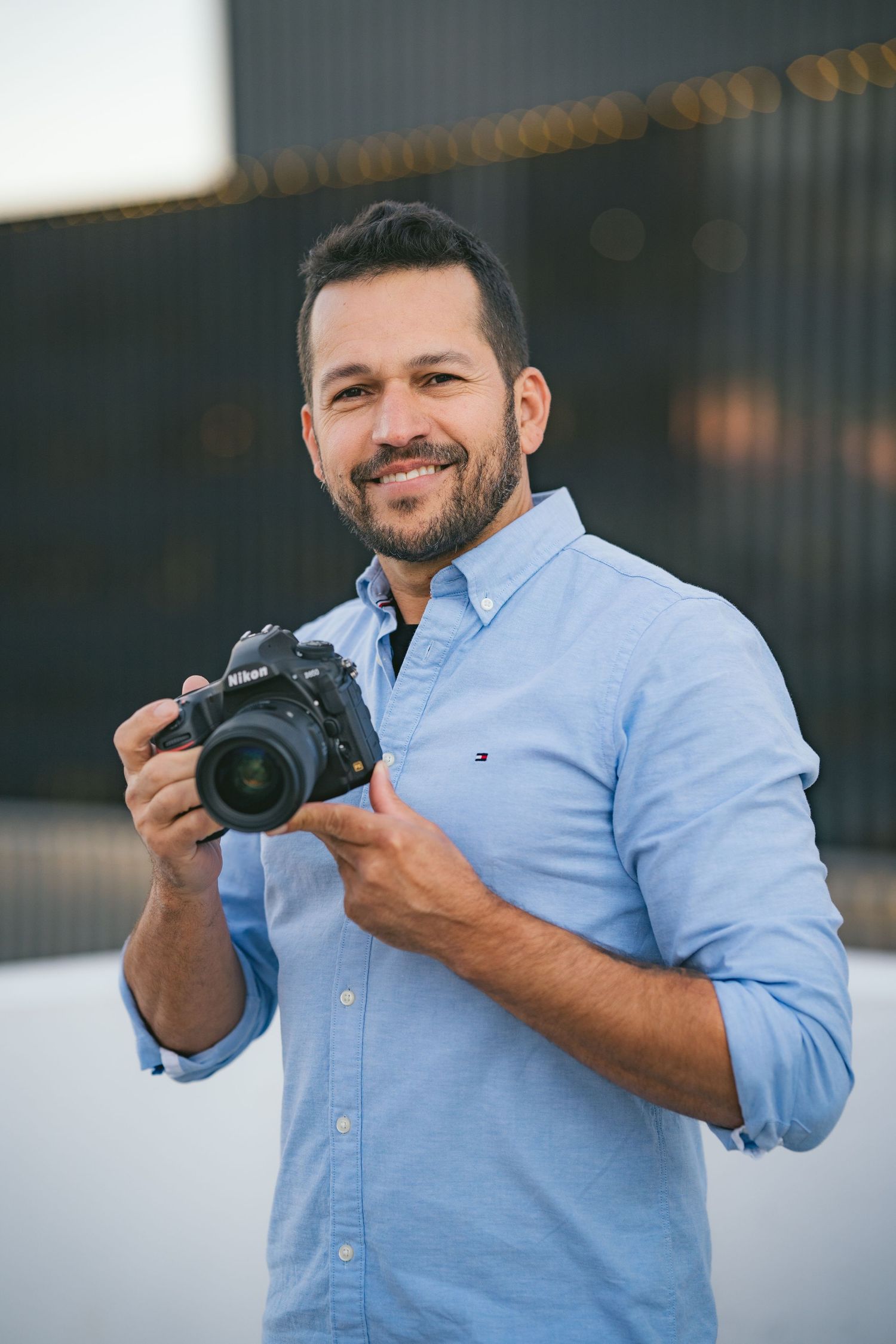 Photographer holding DSLR camera wearing blue button-down shirt.