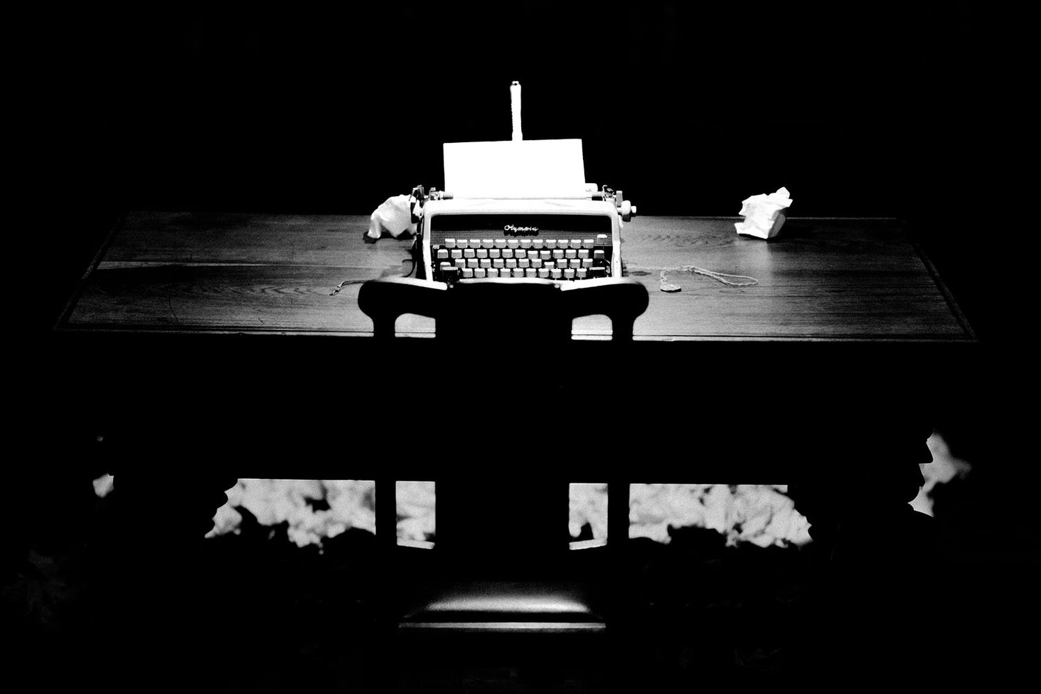 Dark minimalist scene with typewriter silhouetted against black background.