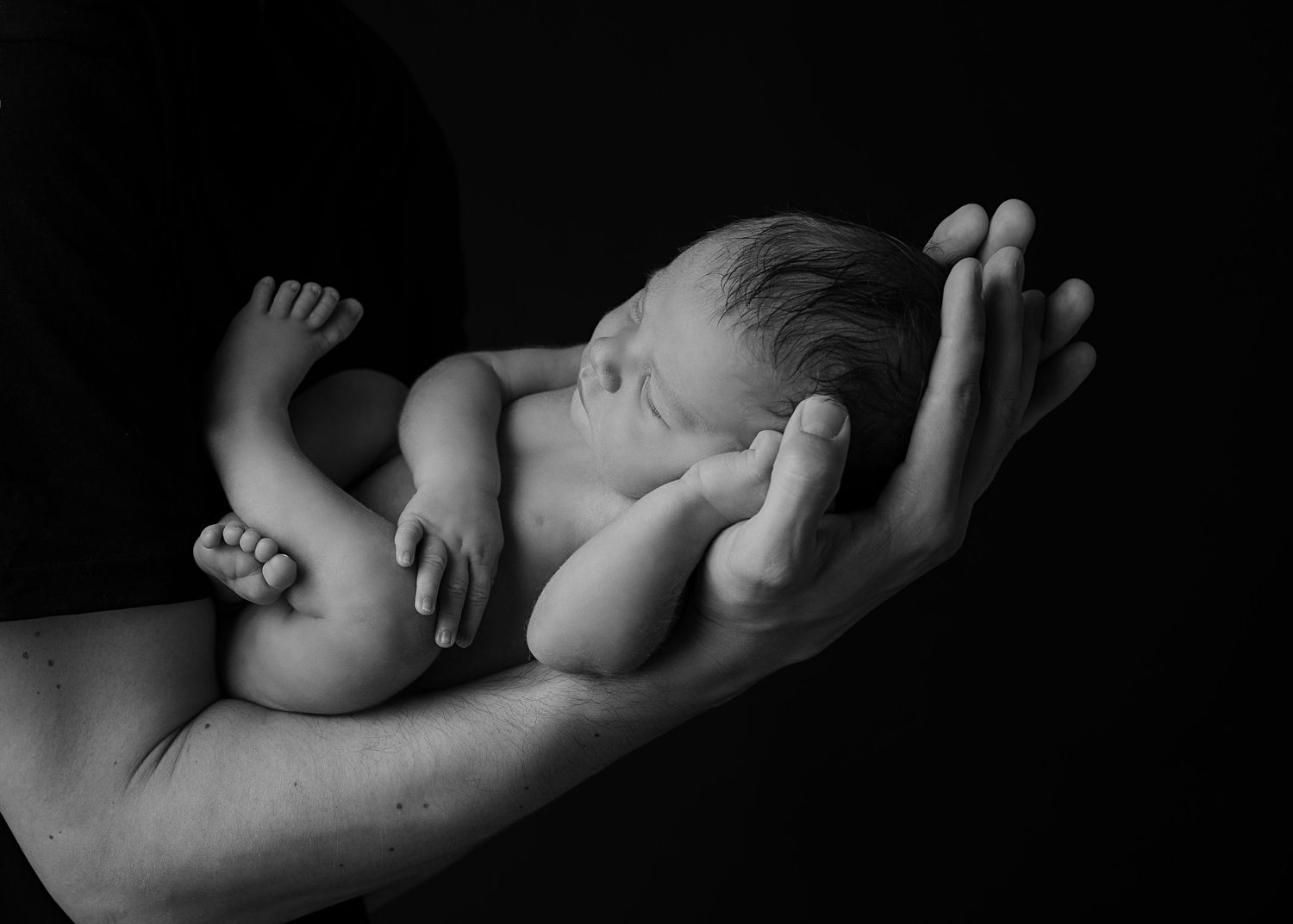Neugeborenes Baby liegt nackt auf Papas Arm bild in schwarz weiß