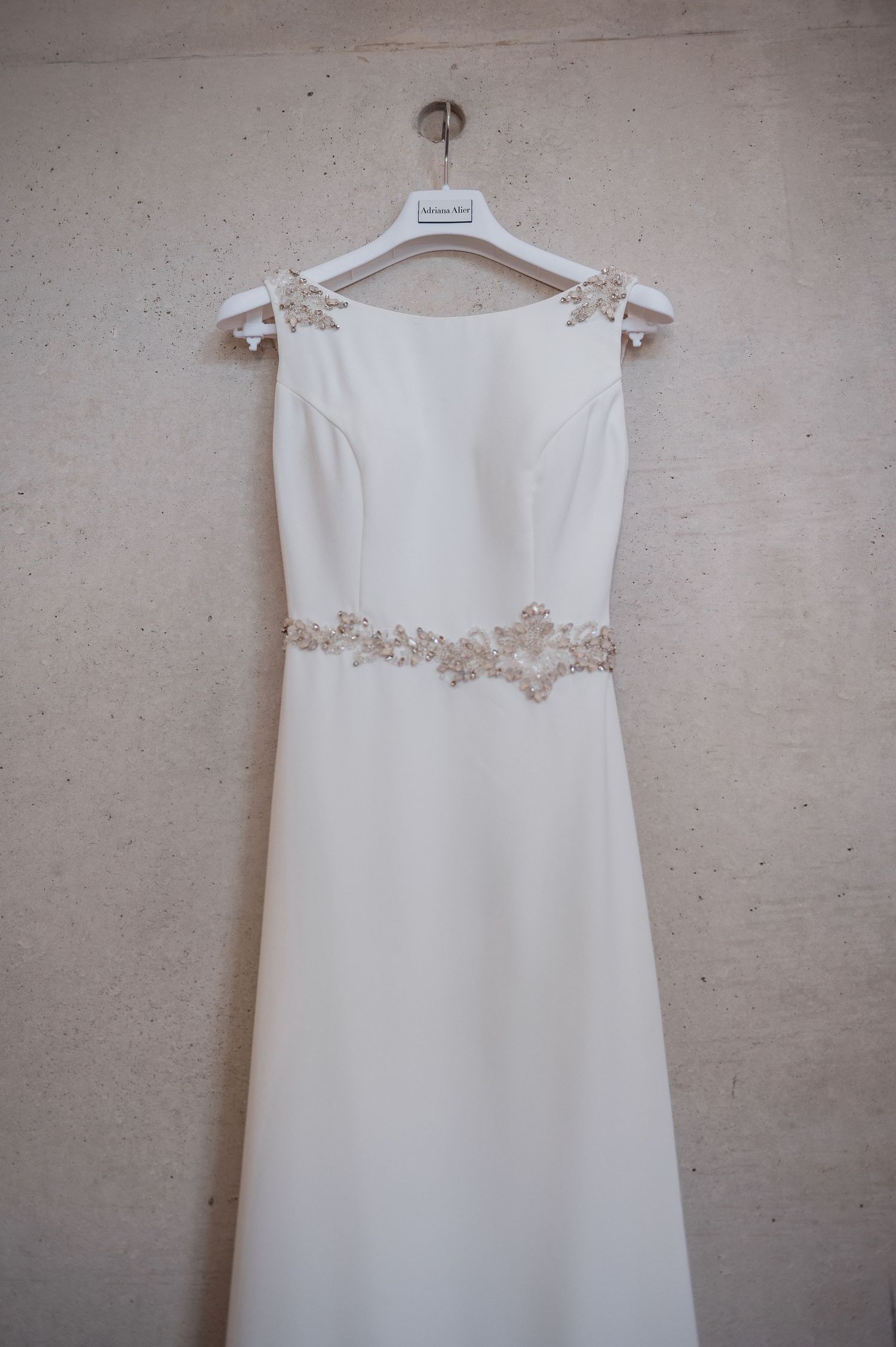 Brautkleid mit Schmucksteinen hängt an Betonwand