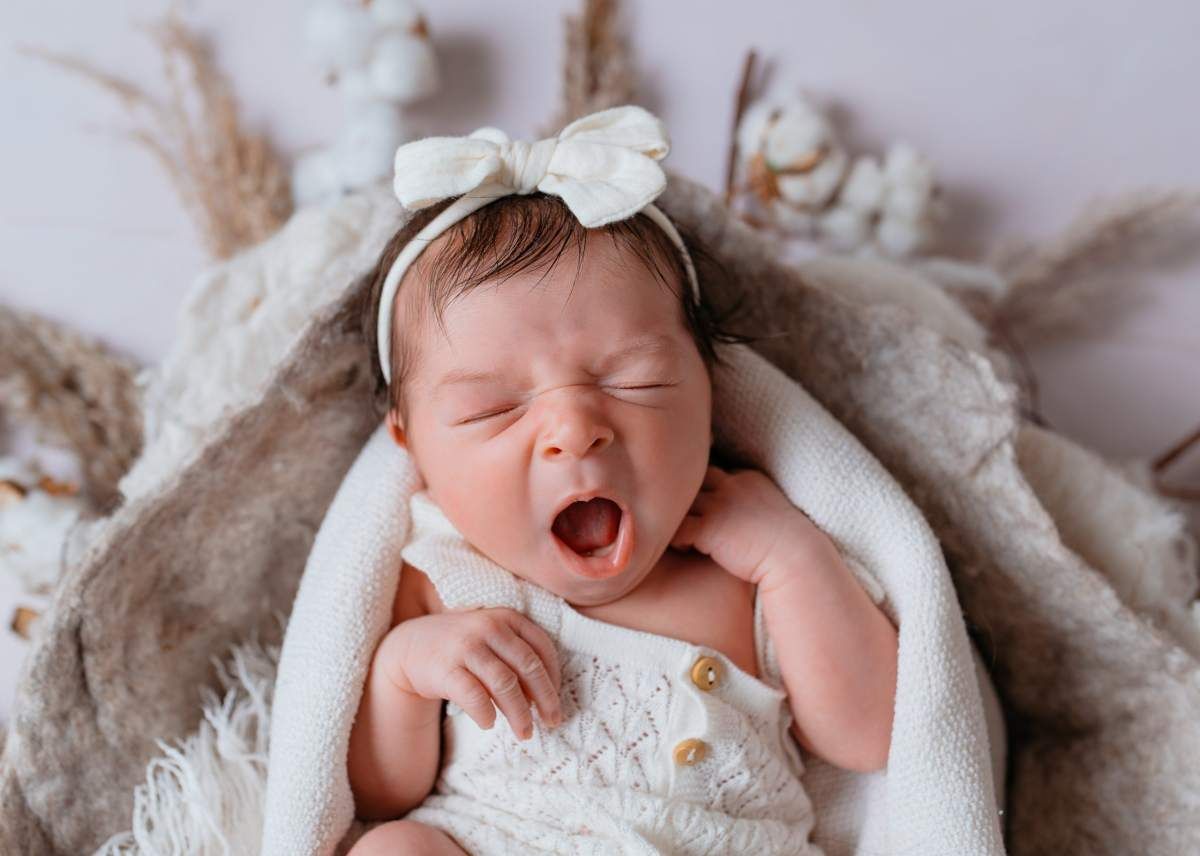 Neugeborenes Baby mit weißer schleife gähnt