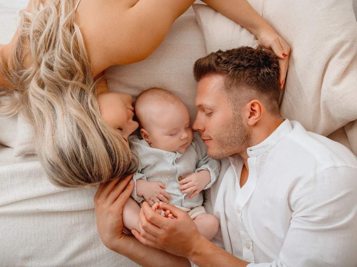 Mama und Papa liegend mit neugeborenem Jungen in der Mitte