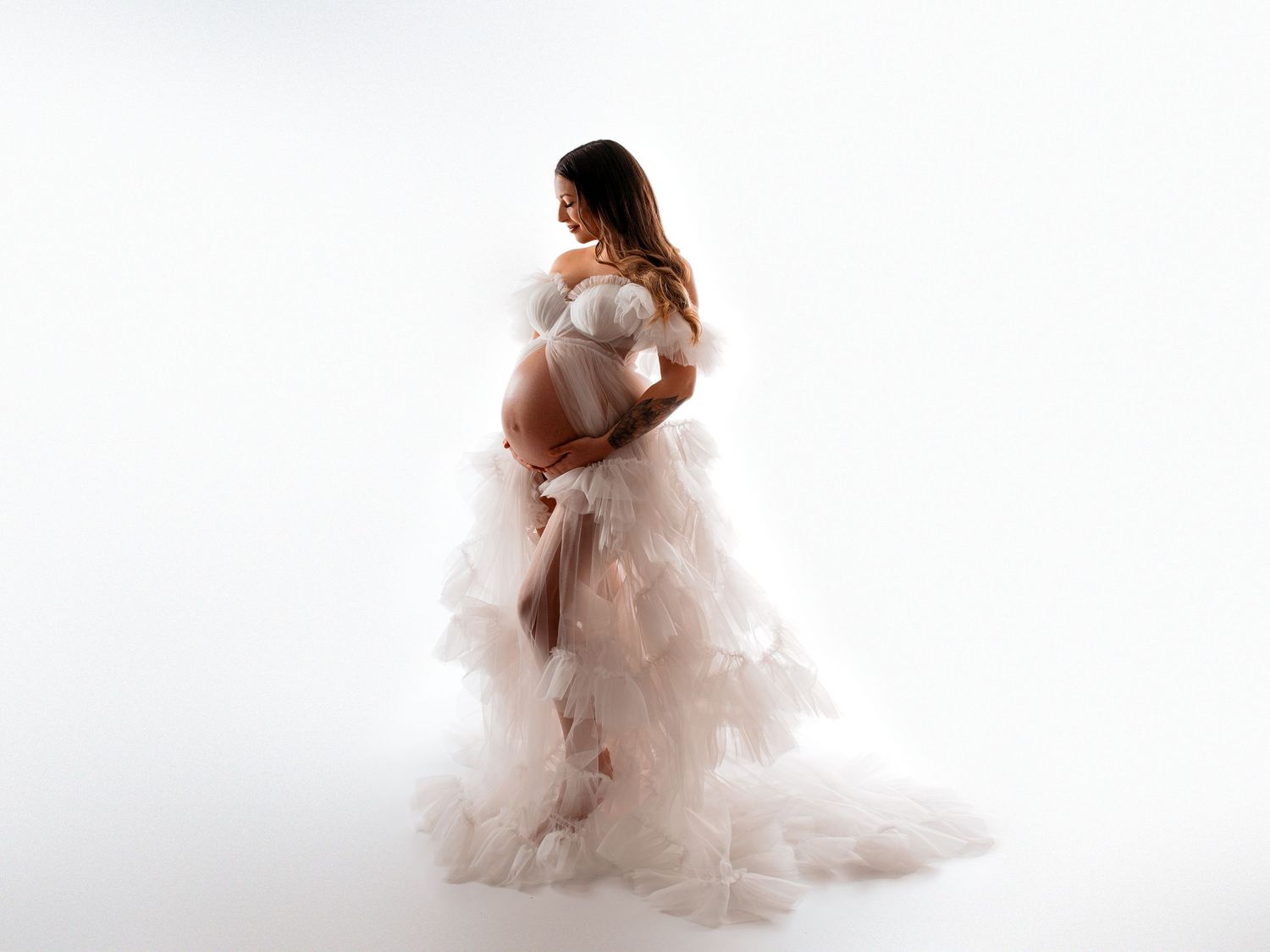 Emotionales Babybauch-Fotoshooting in natürlichem Stil. Frau in Tüllkleid
