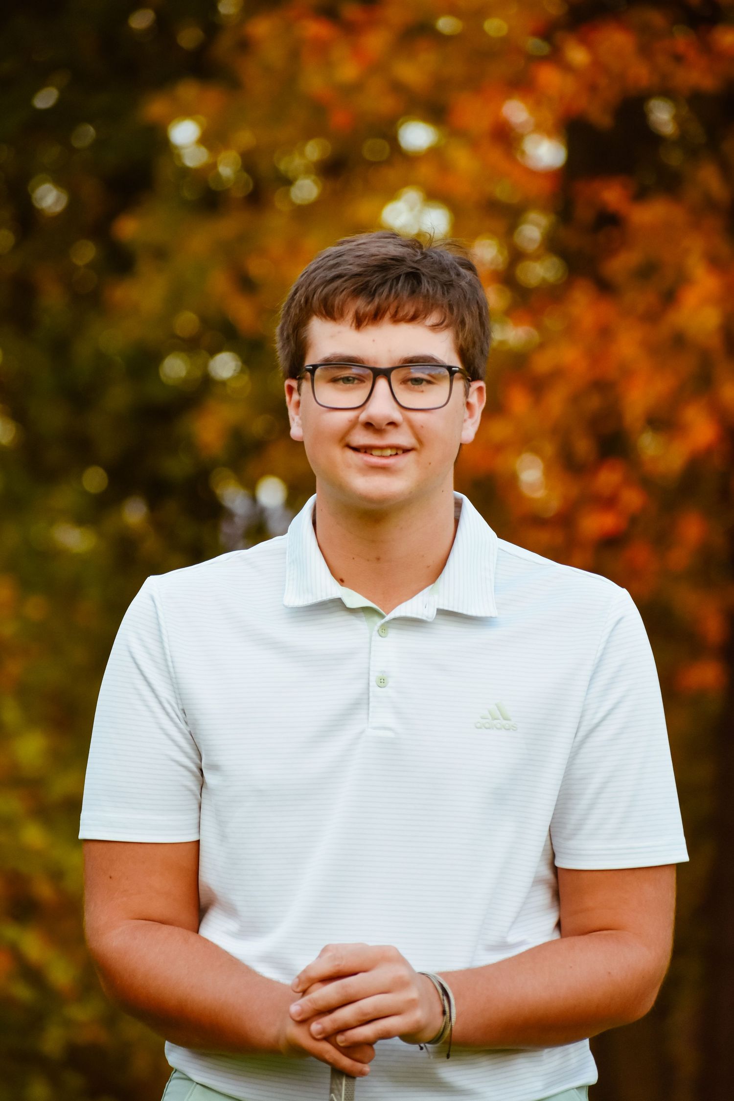 Outdoor portrait in white polo shirt with autumn foliage creating a warm backdrop.