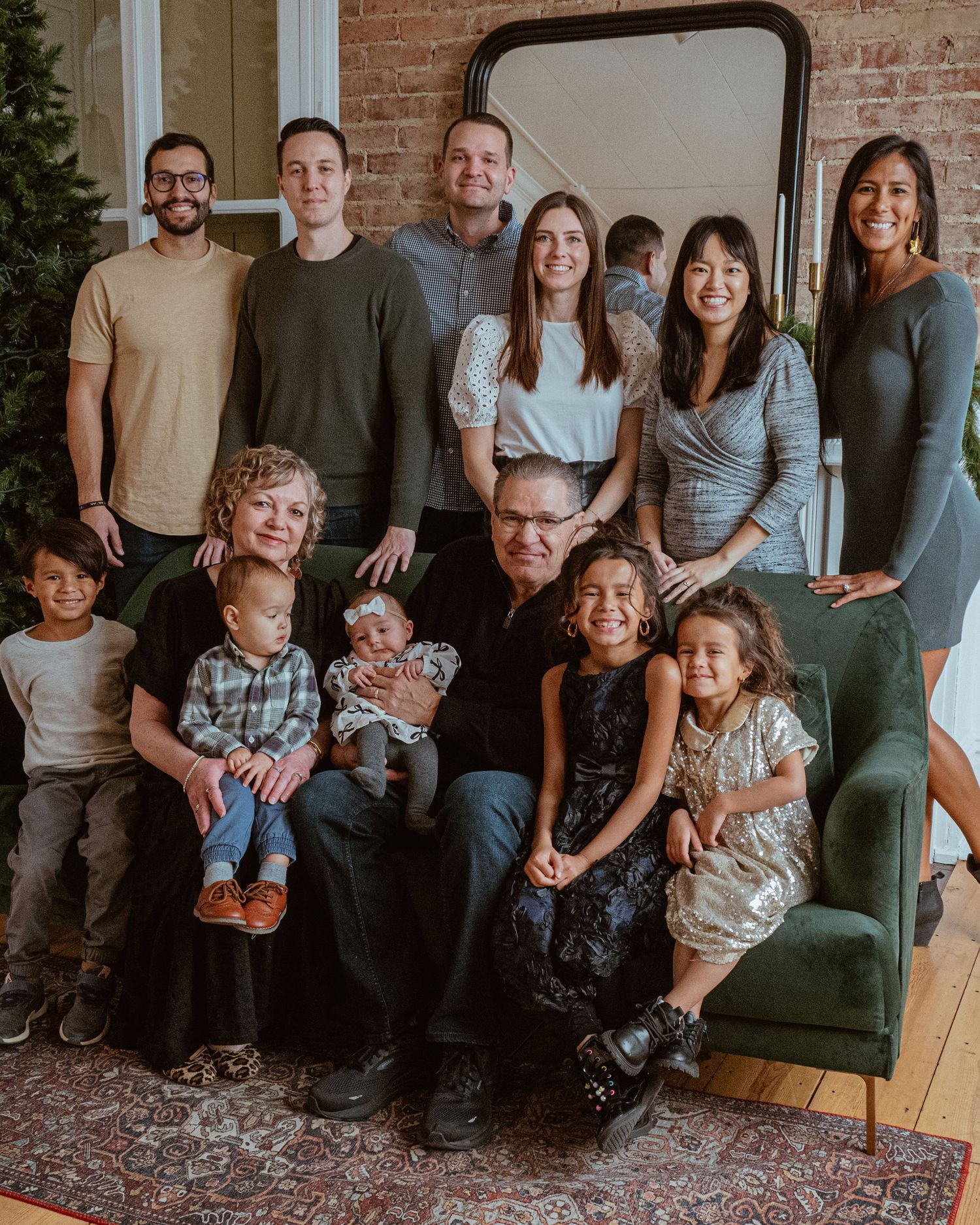 Group photo session with extended family sitting on a green sofa against a rustic brick wall backdrop.