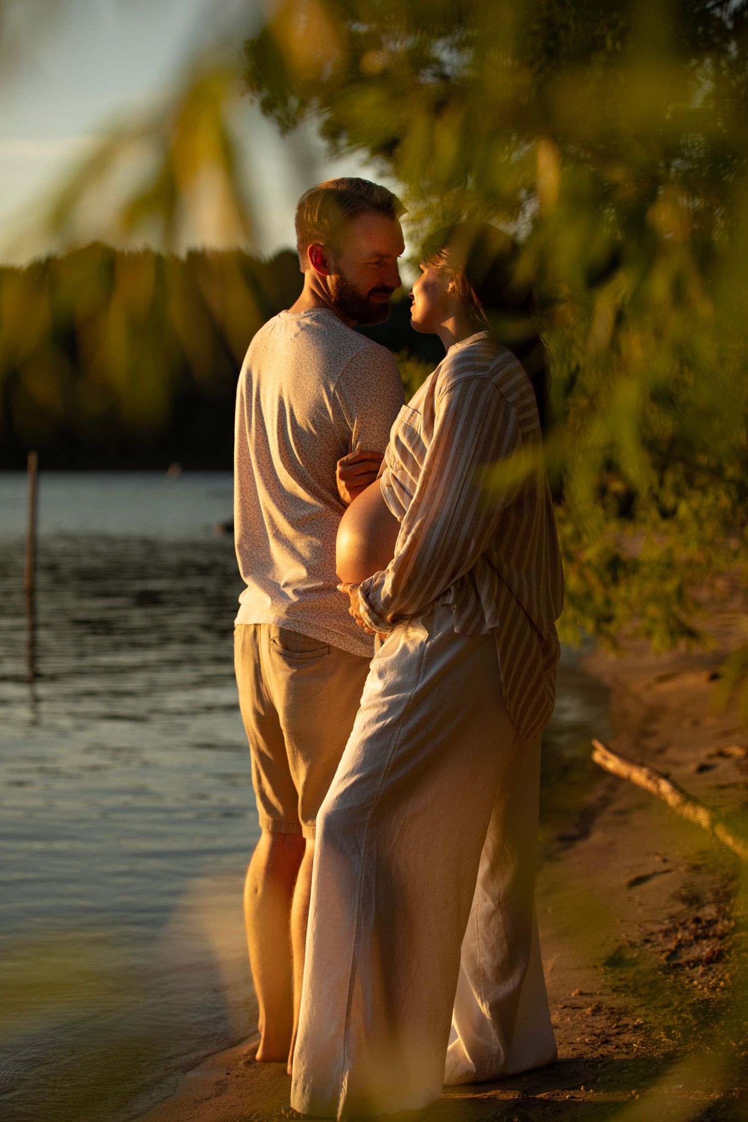 Couple in light colored clothing embracing by lakeside during golden sunset.