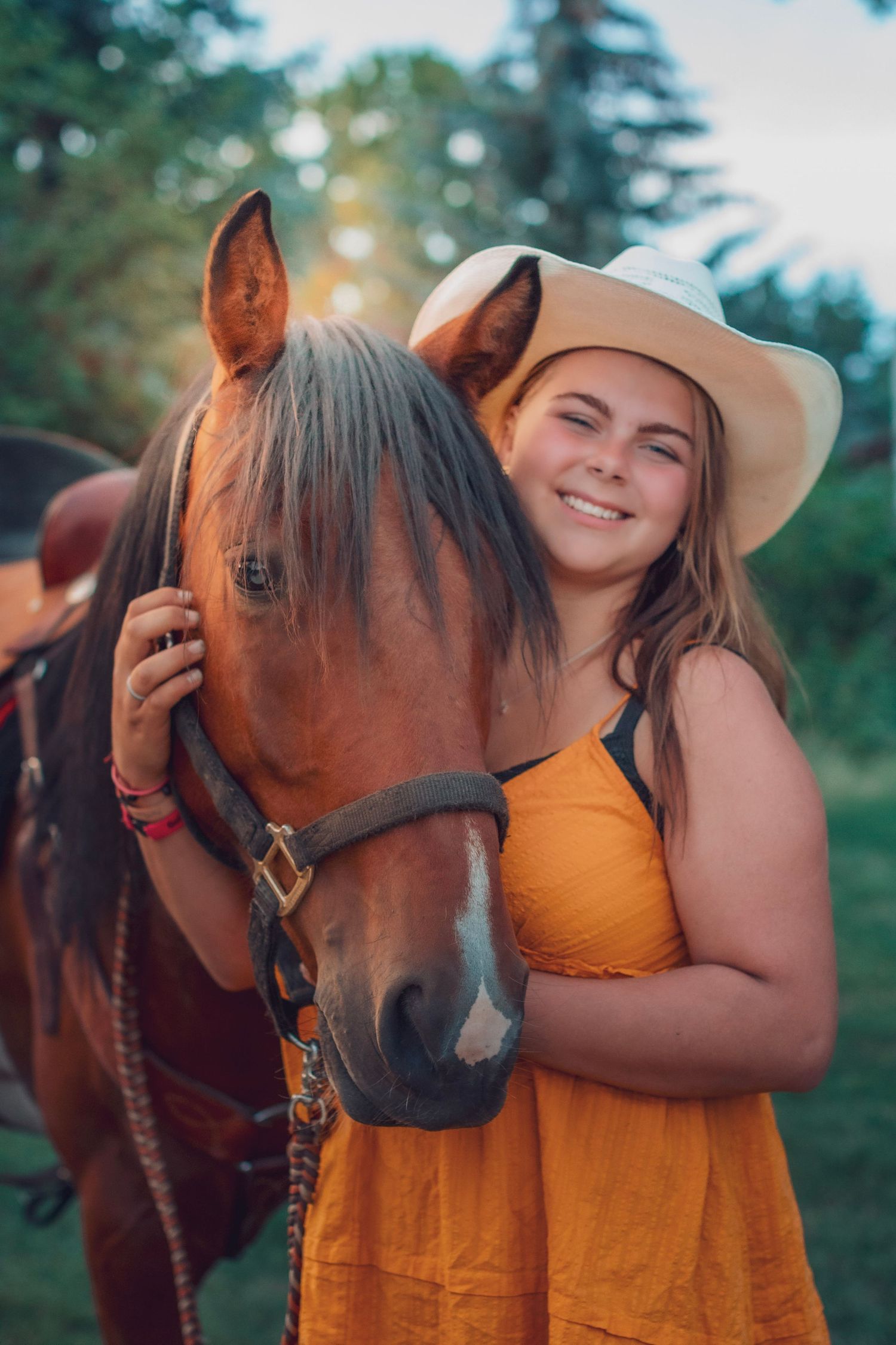A person in an orange dress hugging a brown horse outdoors on a summer day.