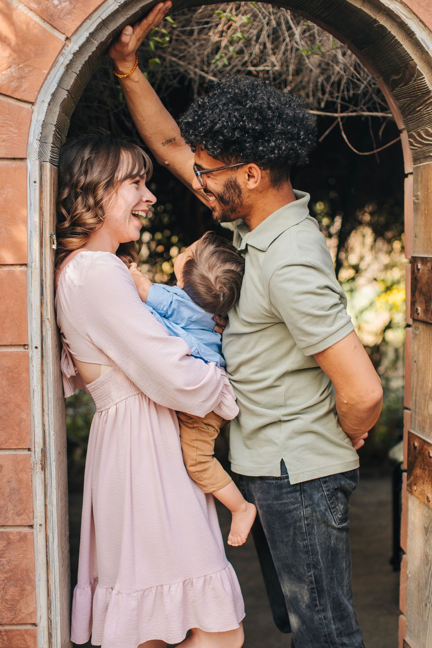 A sweet family moment captured under a brick archway in soft natural lighting.