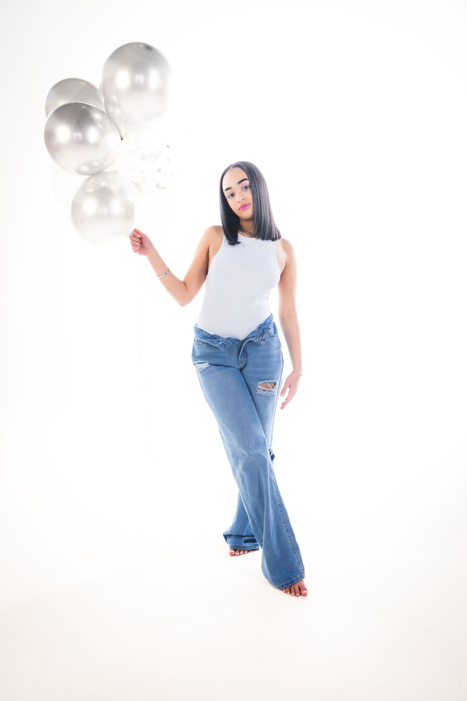 Casual pose with silver balloons wearing white tank top and distressed jeans.