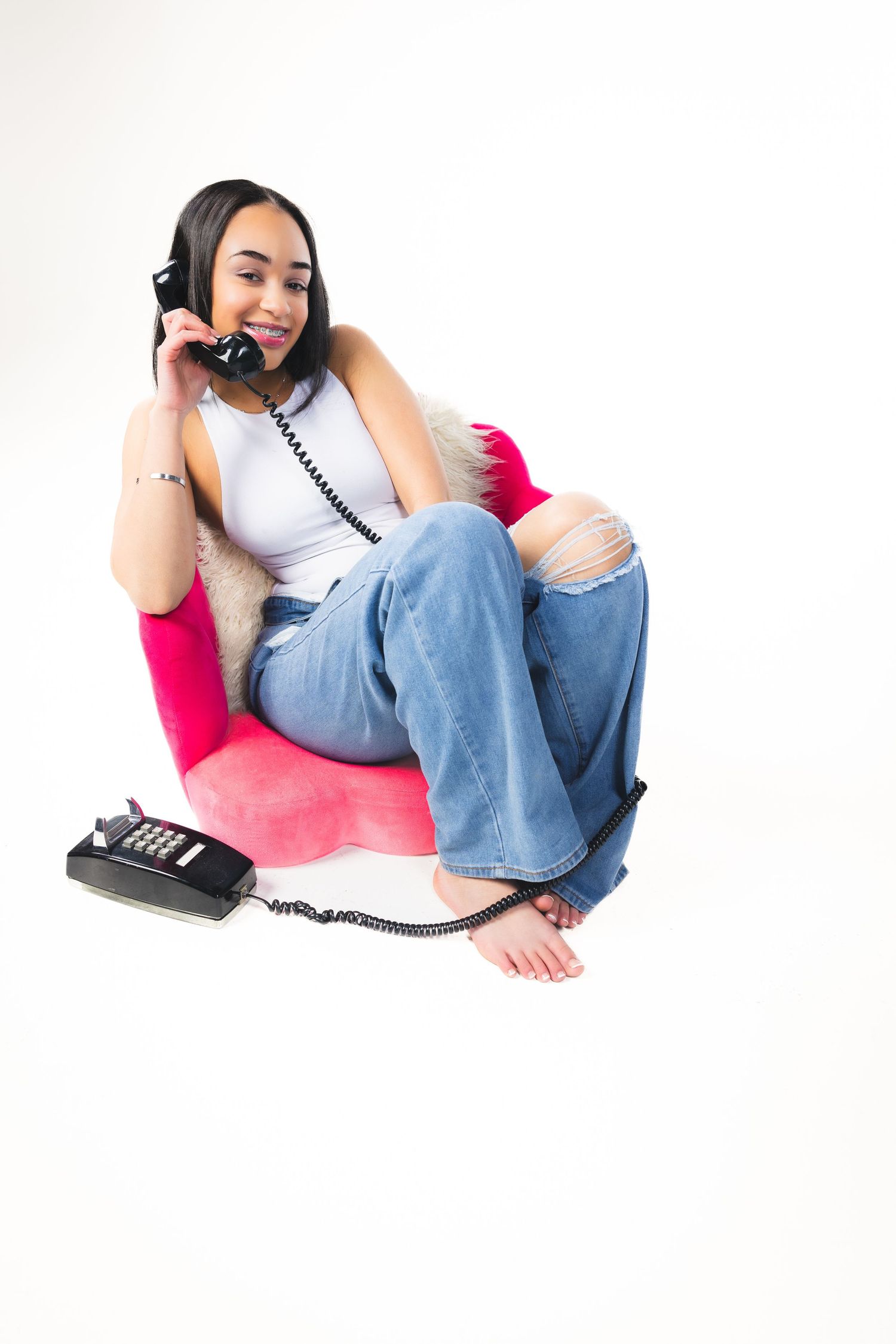 Casual portrait talking on retro telephone while lounging in pink chair.