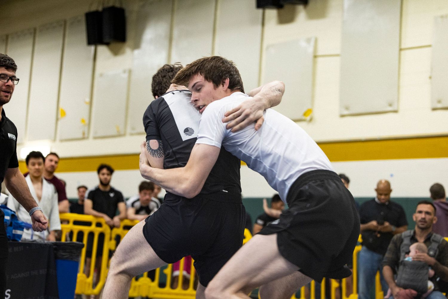 Two wrestlers grapple during an intense high school match as spectators watch from the sidelines.