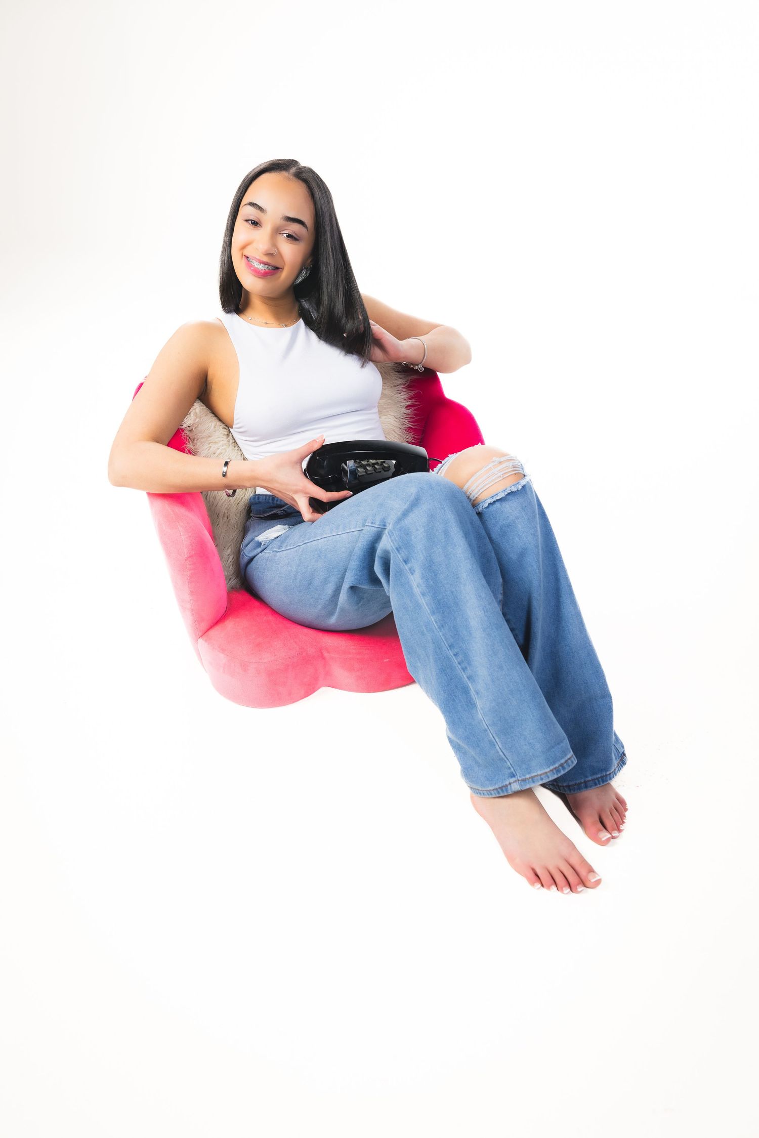 Young person relaxes in a pink bean bag chair wearing casual jeans and white tank top.