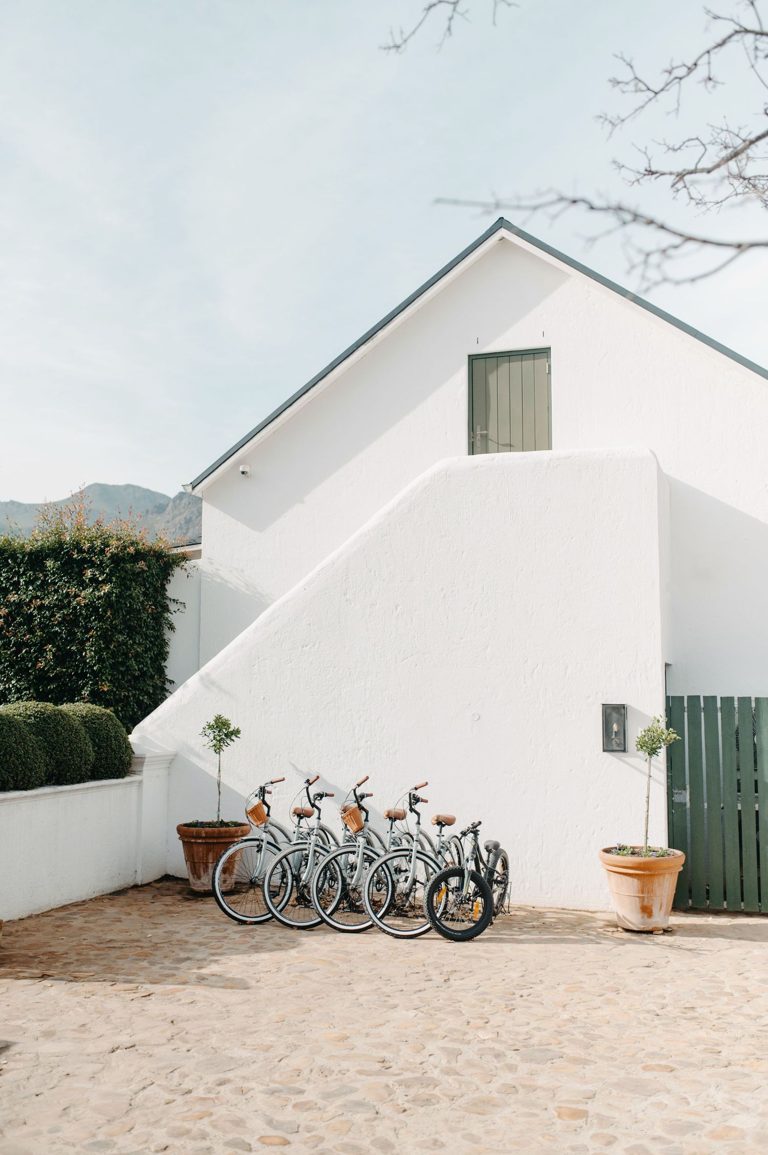 Row of bicycles parked against a white stucco wall of a Mediterranean-style building with mountains in background.