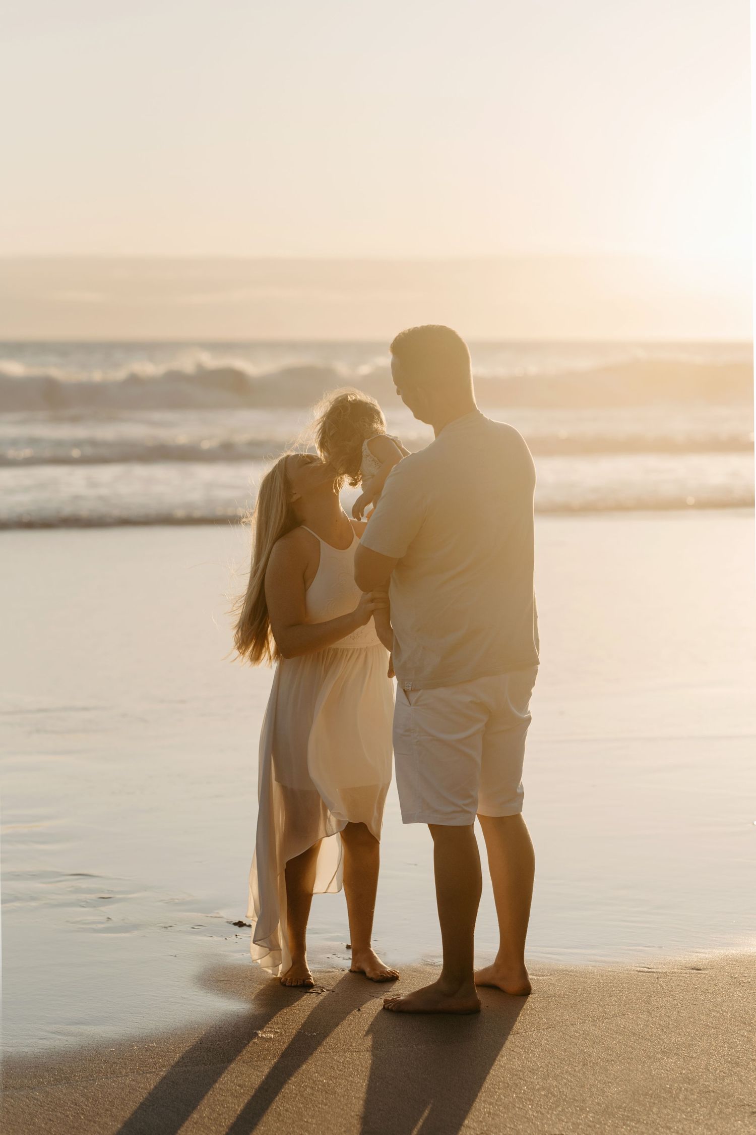 A couple stands silhouetted on a beach at sunset, looking out at the ocean waves in romantic golden light.
