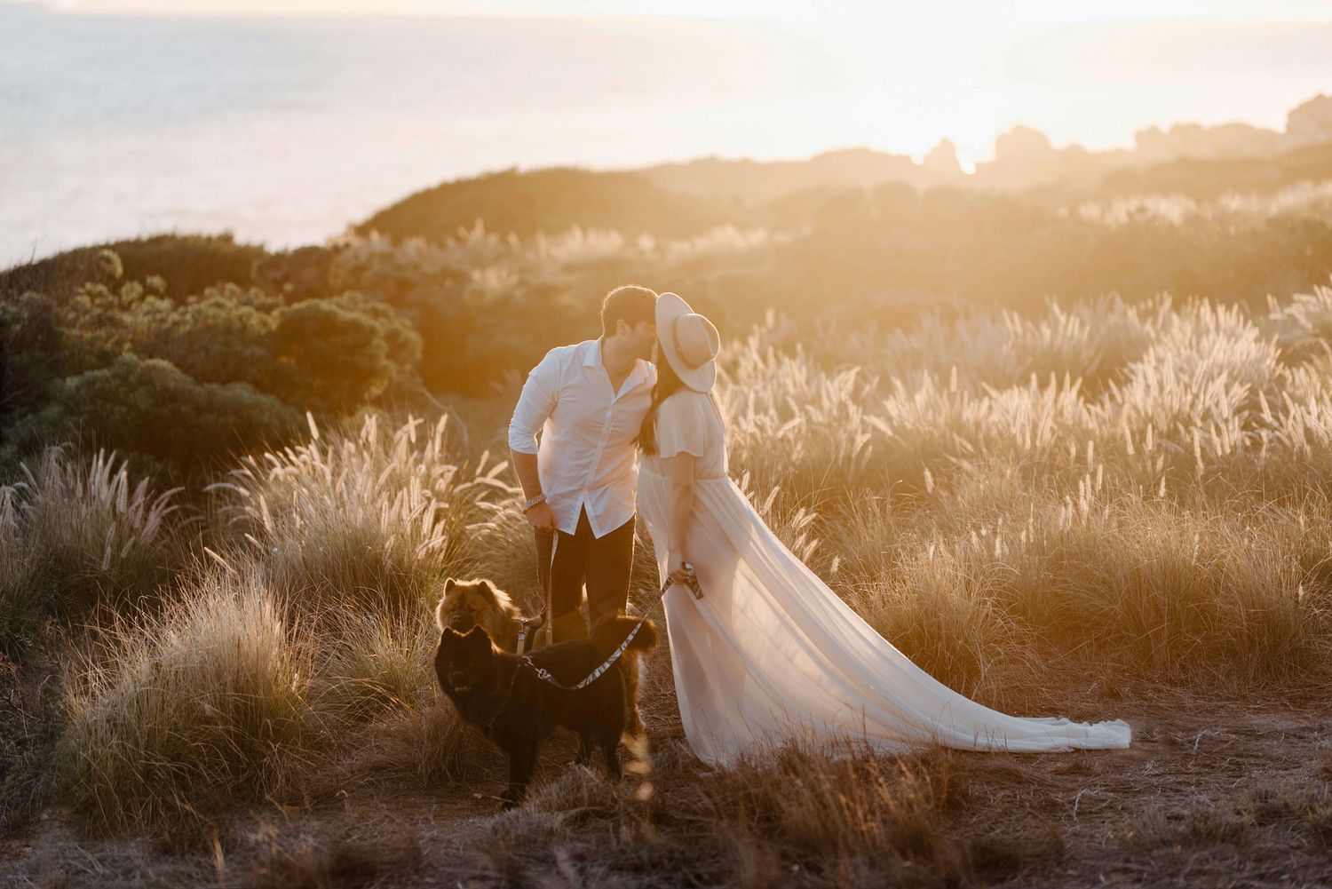 A romantic couple embraces in tall golden grass at sunset creating a dreamy silhouette against the glowing sky.