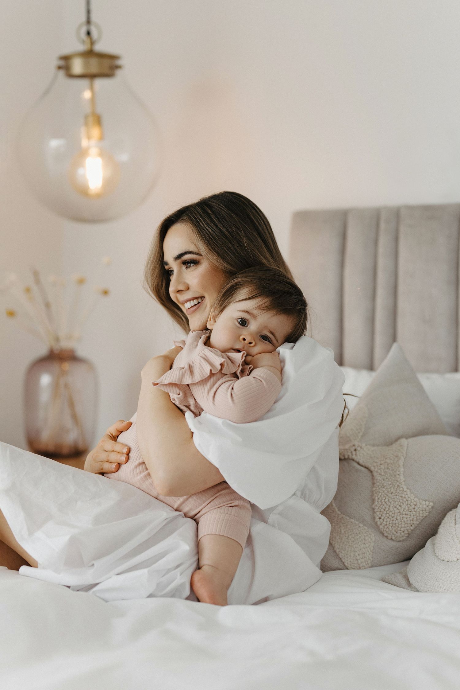 A tender moment captured in white bedding with a pendant light glowing warmly overhead.