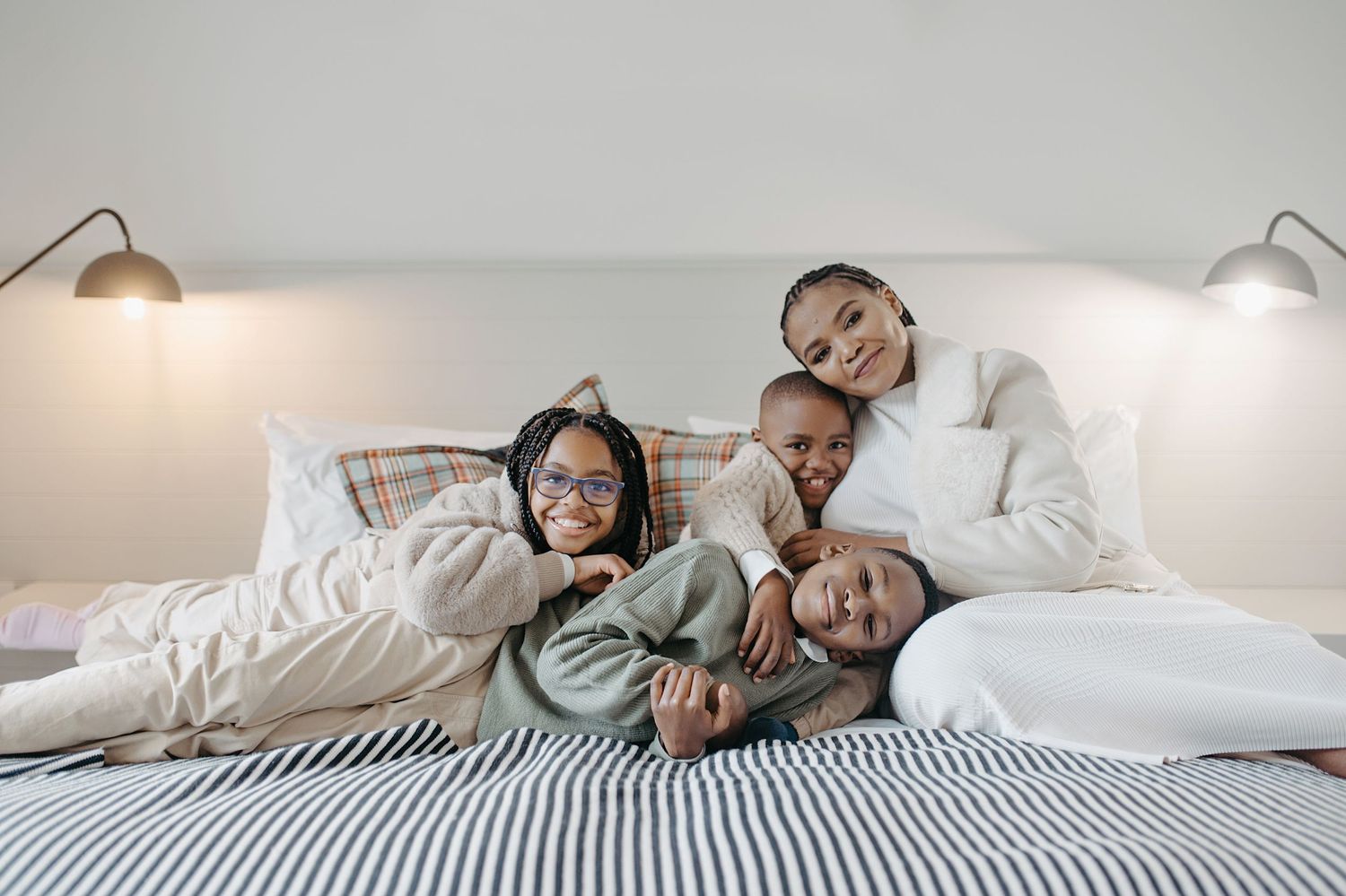 A family snuggles together on a bed with white linens and striped bedding while sharing joyful laughter.