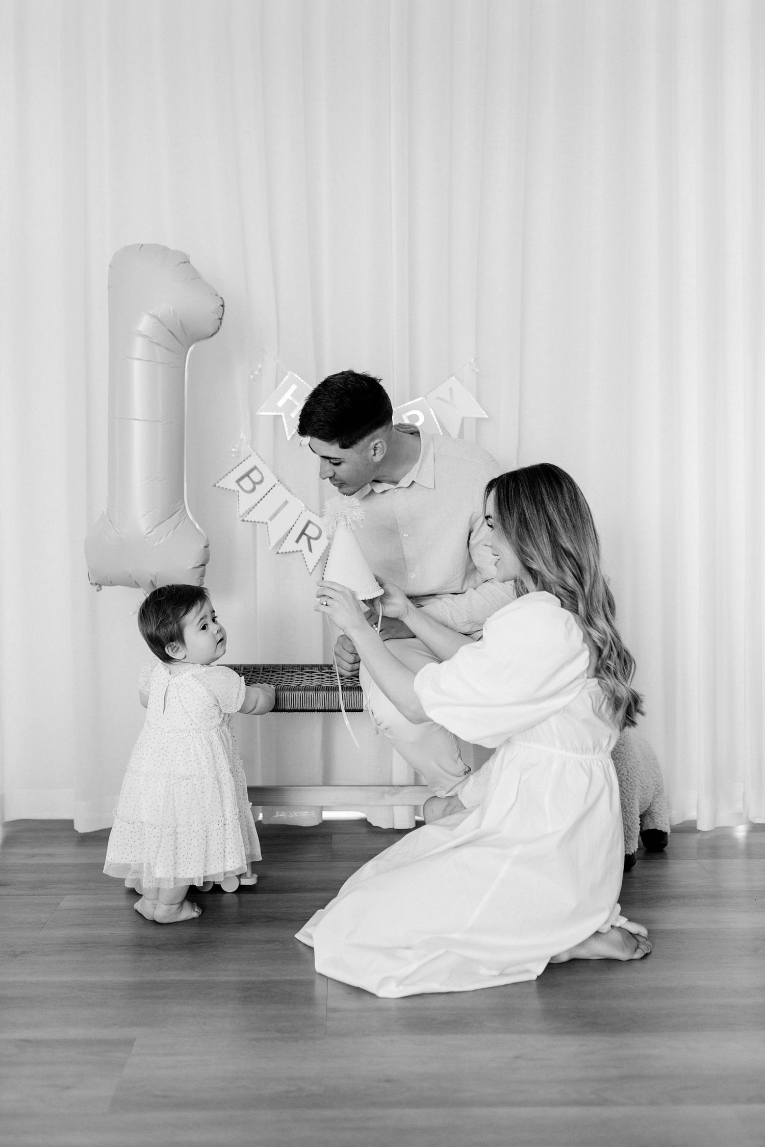 A family celebrates with decorative balloon letters during an intimate black and white portrait session.