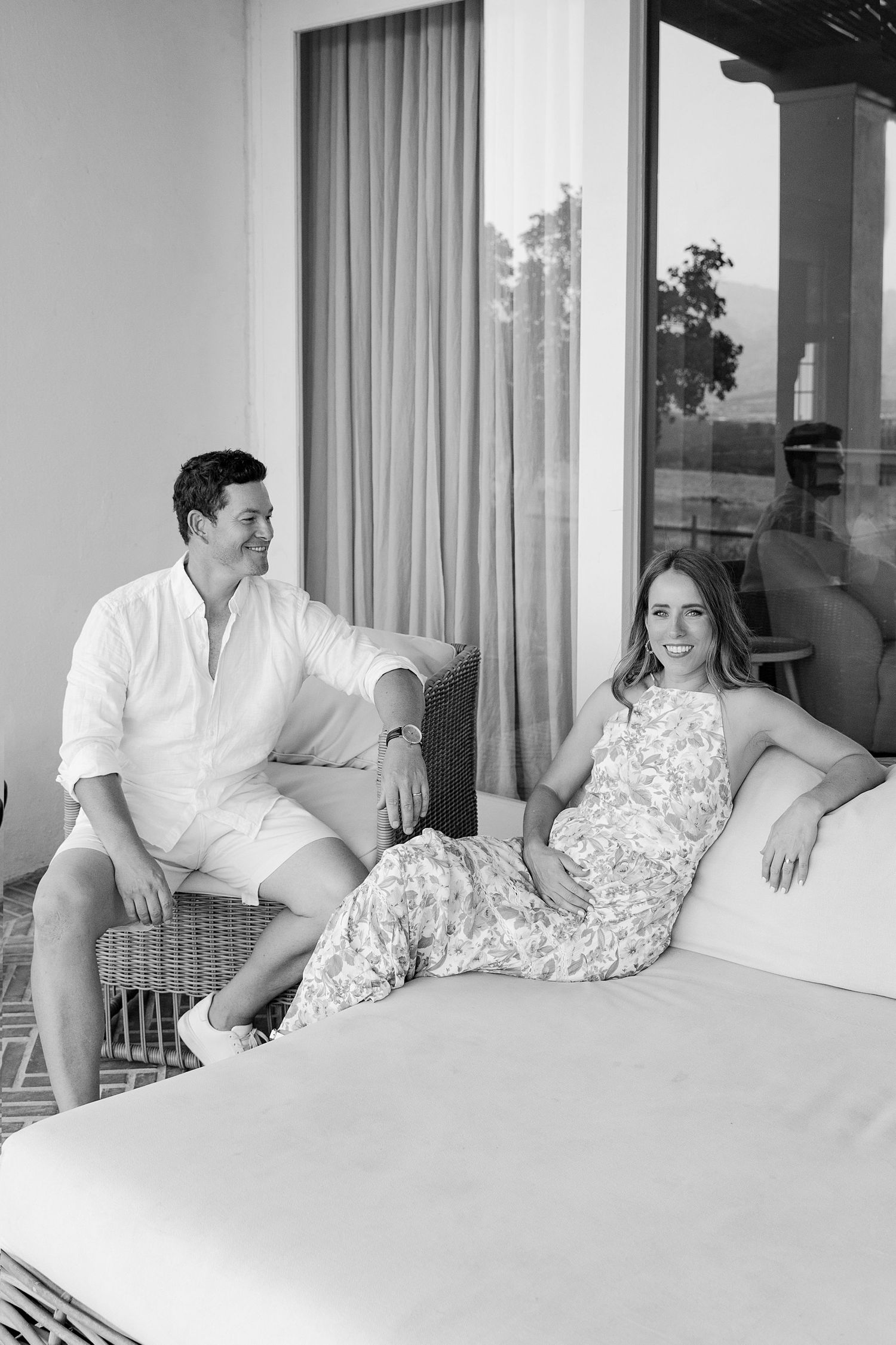 Black and white portrait of couple lounging on outdoor patio furniture.