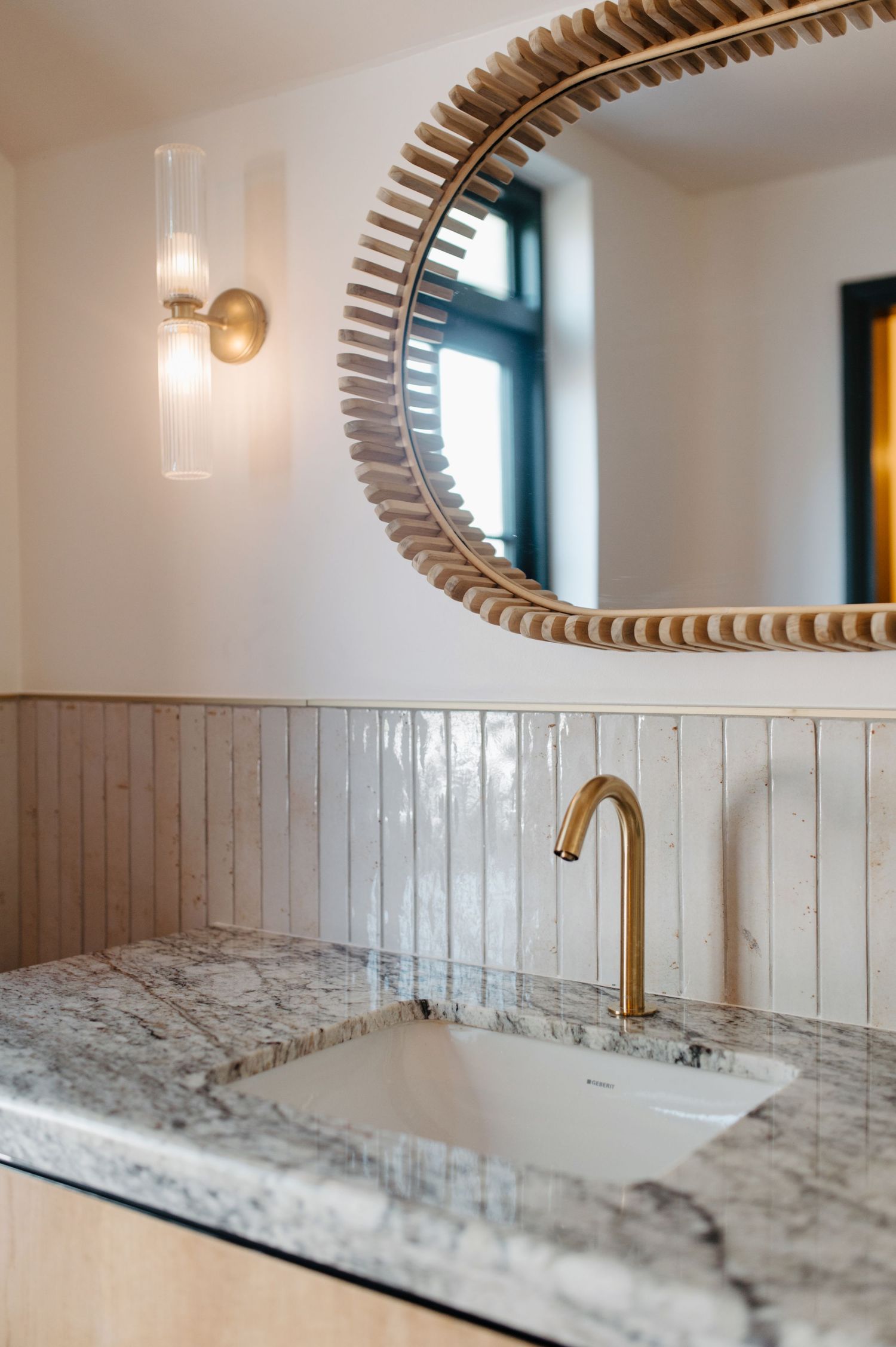 Modern bathroom vanity featuring brass faucet, marble countertop, white beadboard and decorative oval mirror with scalloped frame.
