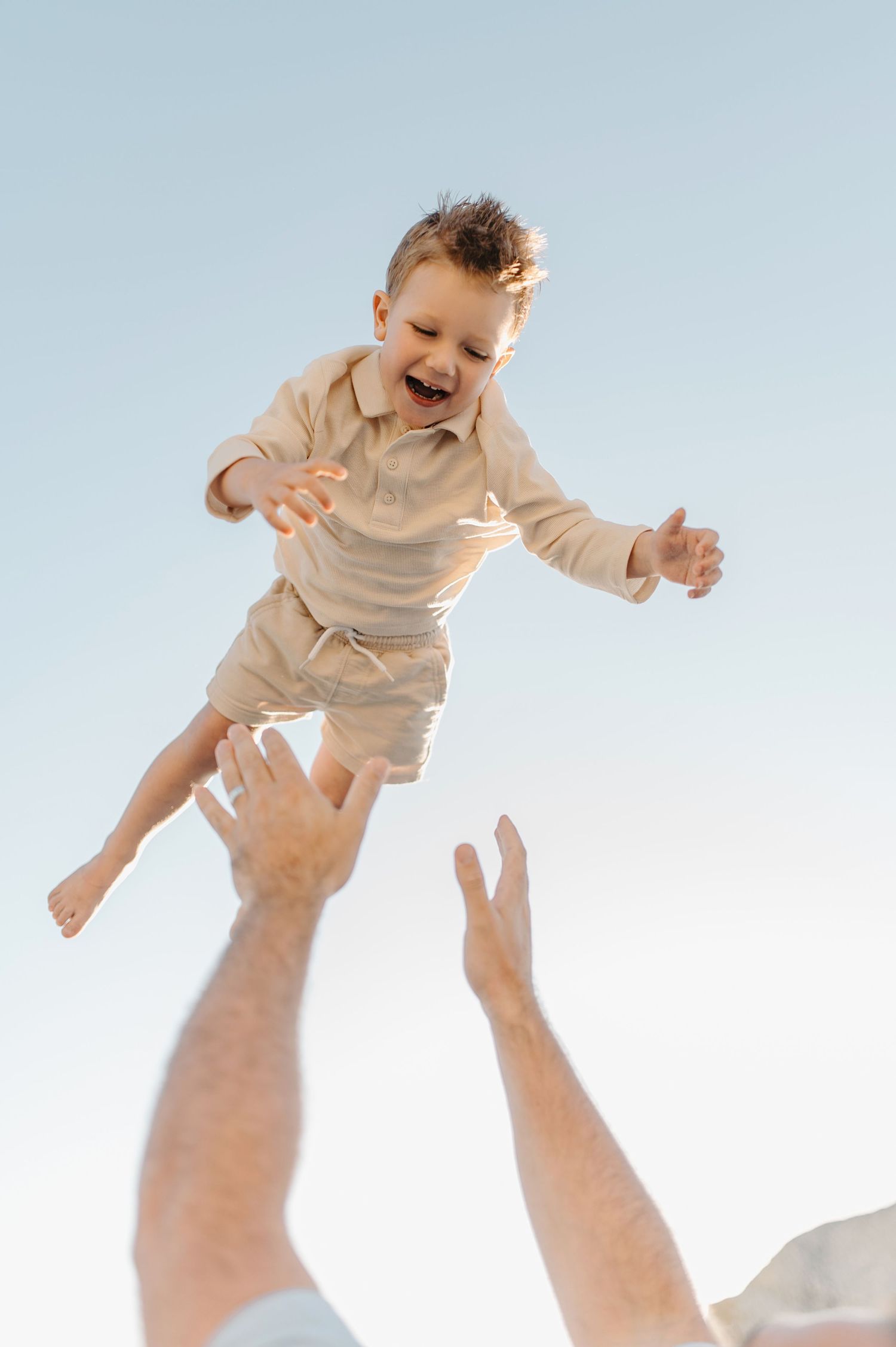 Person holds up infant in a beige outfit against bright sky creating joyful airborne moments in sequence.