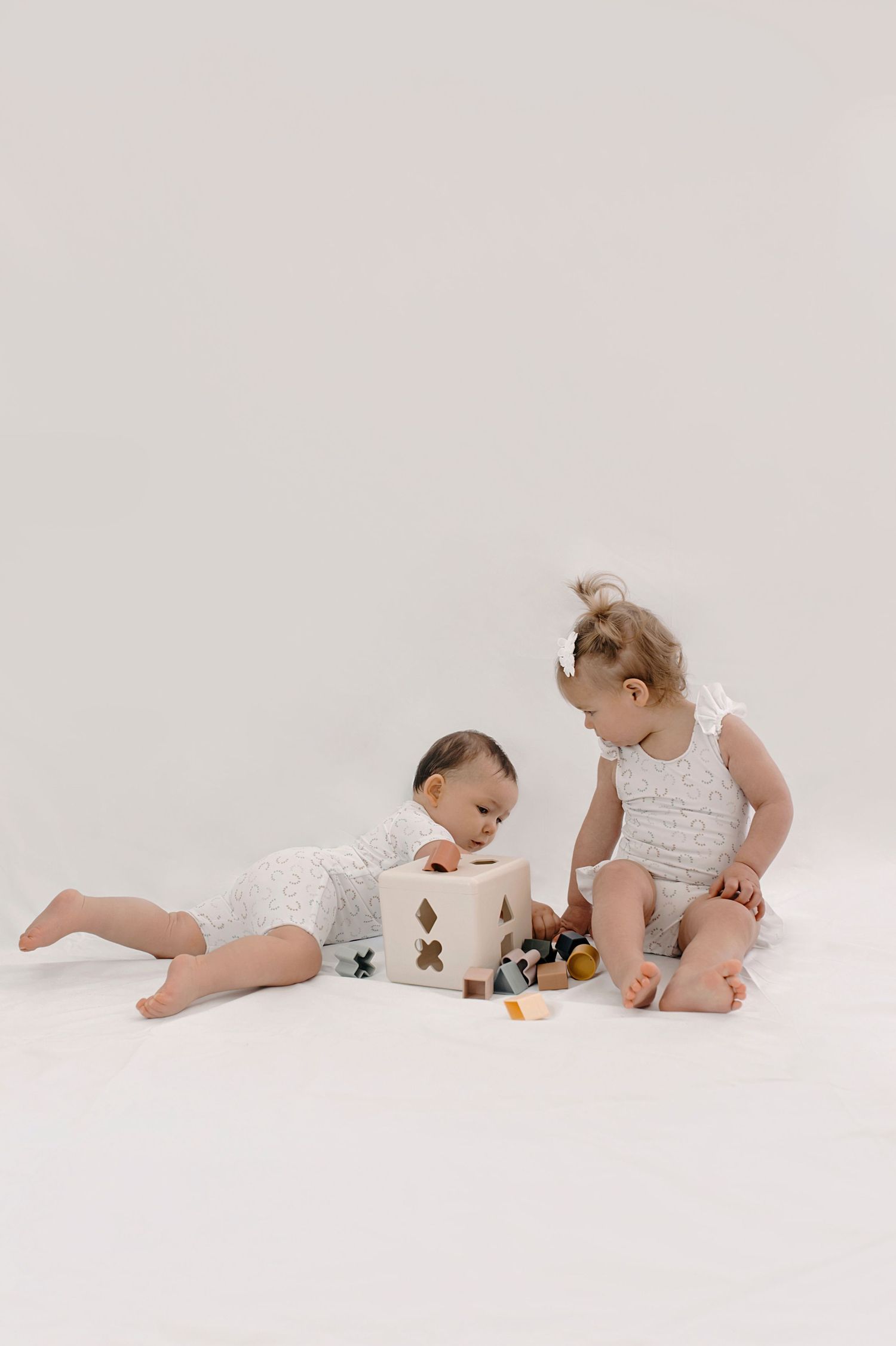 Baby in white onesie plays with toys and rolls on clean white surface in sequence of developmental stages.