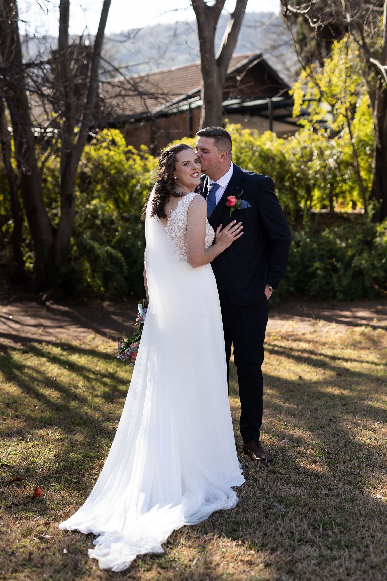 A romantic outdoor winter wedding scene with sunlit trees creating a magical atmosphere in the background.