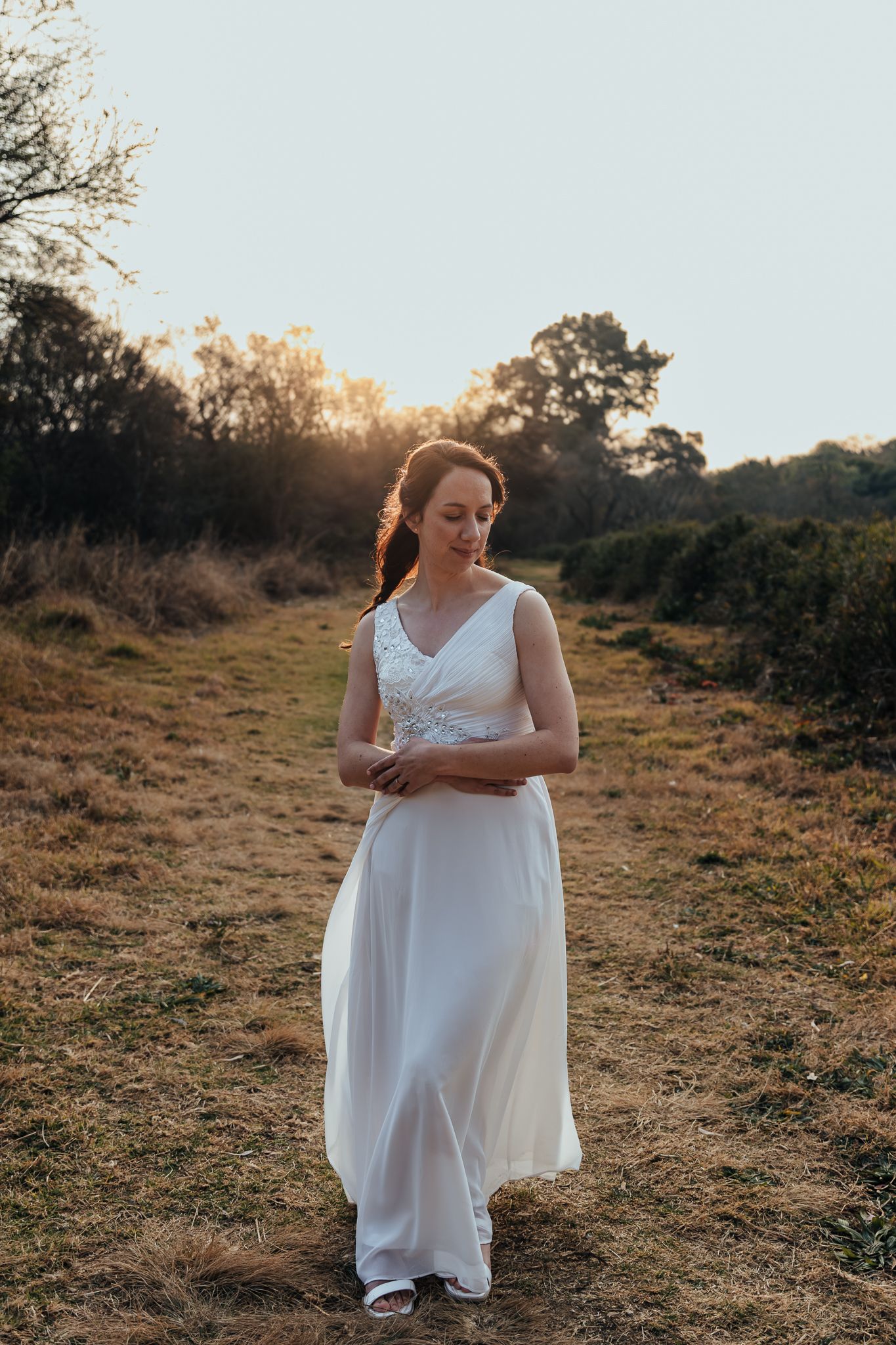 Person in flowing white dress standing on golden hillside during sunset photoshoot.