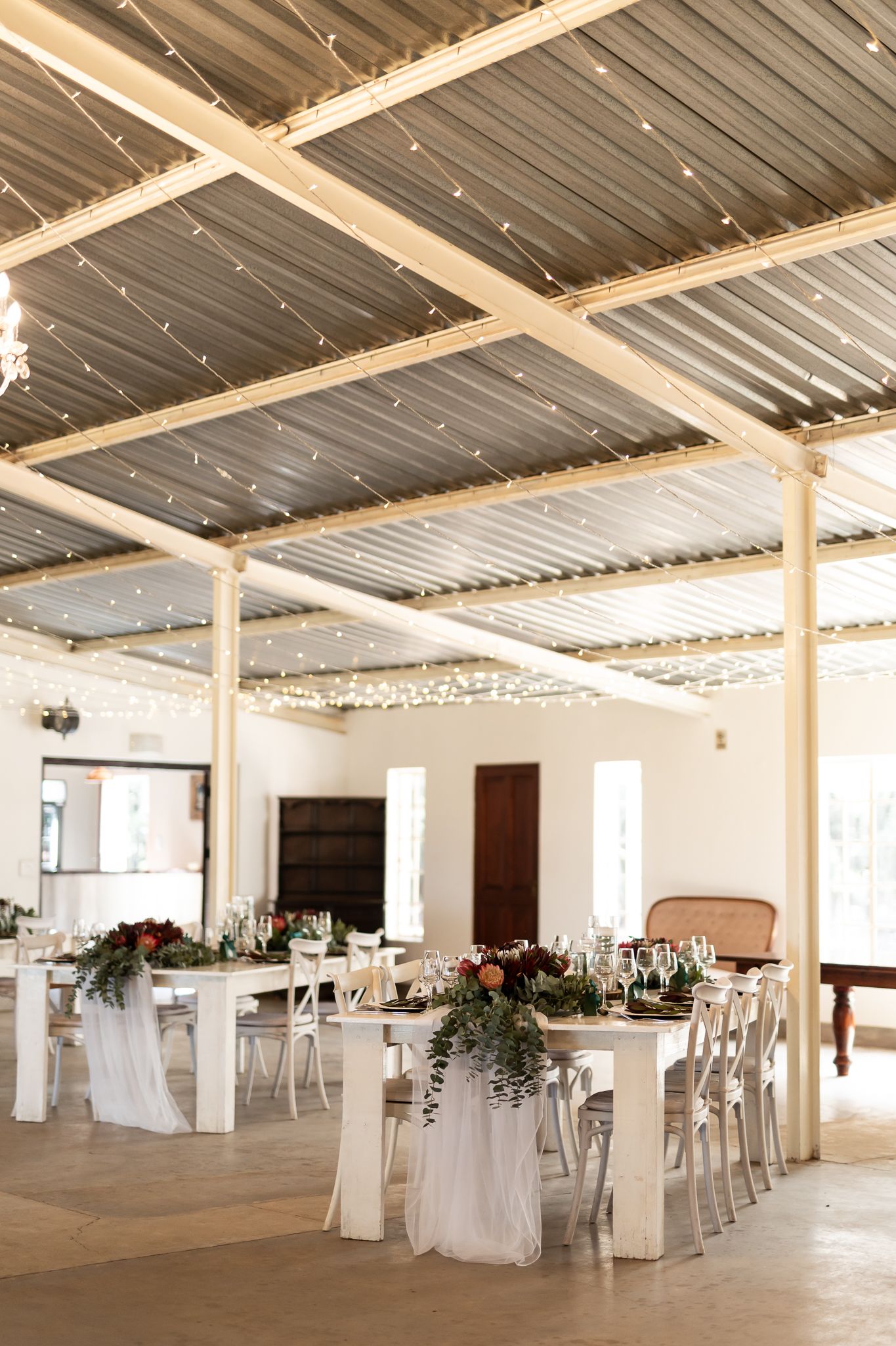 Wedding reception hall with industrial ceiling, string lights, and white-draped tables.