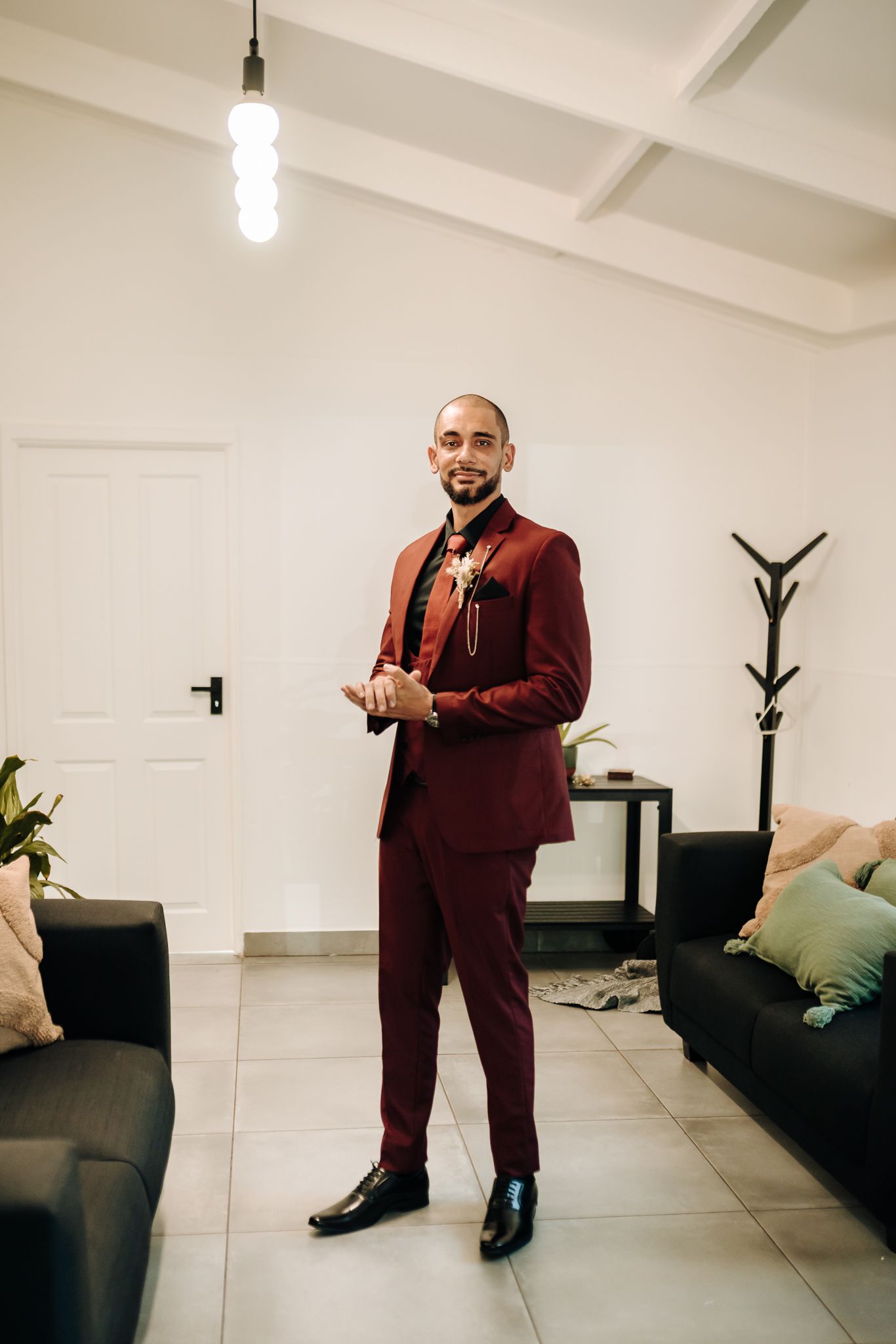 Person in burgundy suit standing in modern living room with pendant lighting.