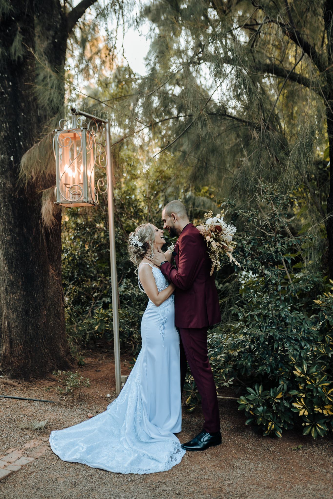 Elegant wedding couple embraces under vintage lantern in forest setting.