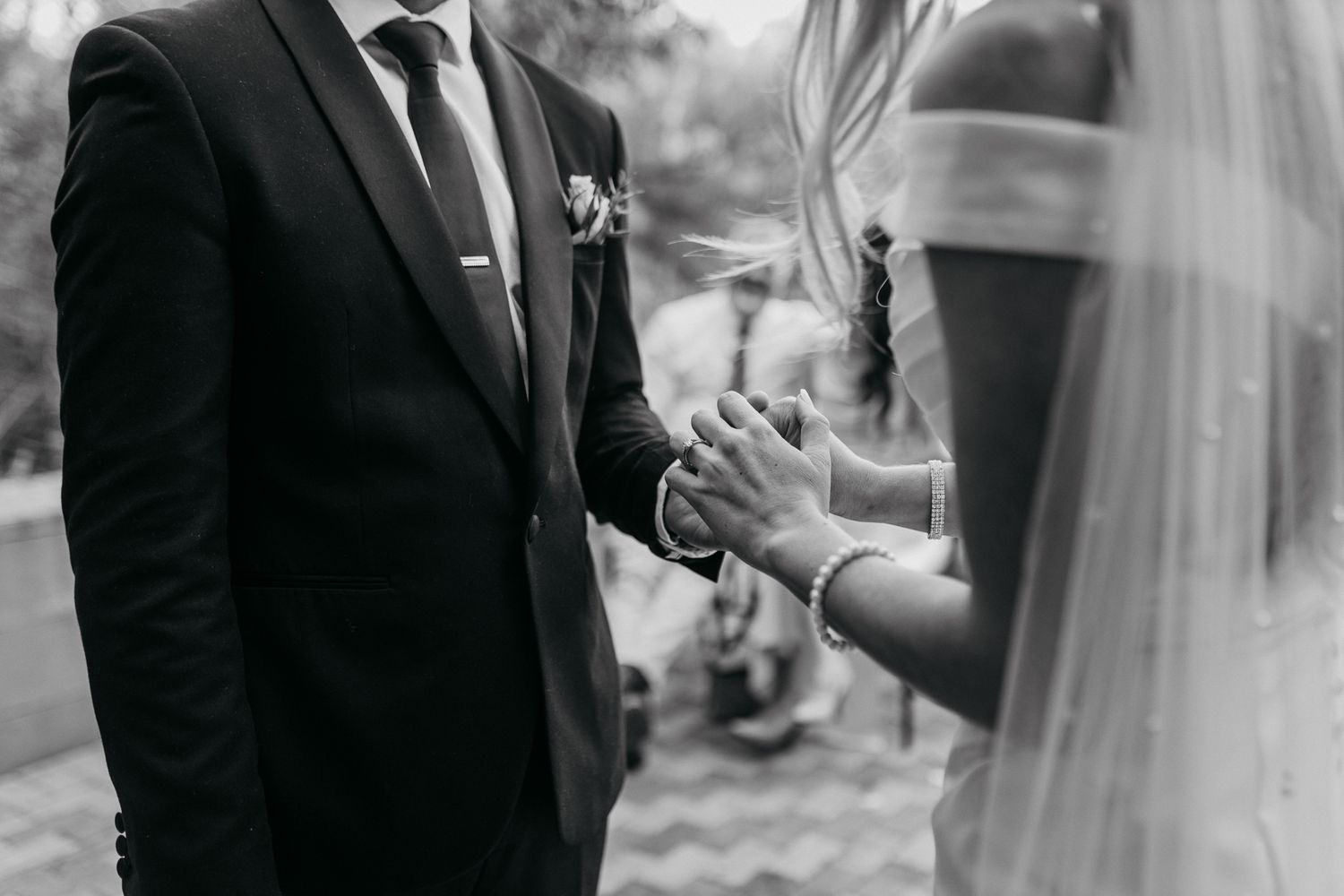Black and white photo of a tender moment between newlyweds holding hands during their wedding ceremony.