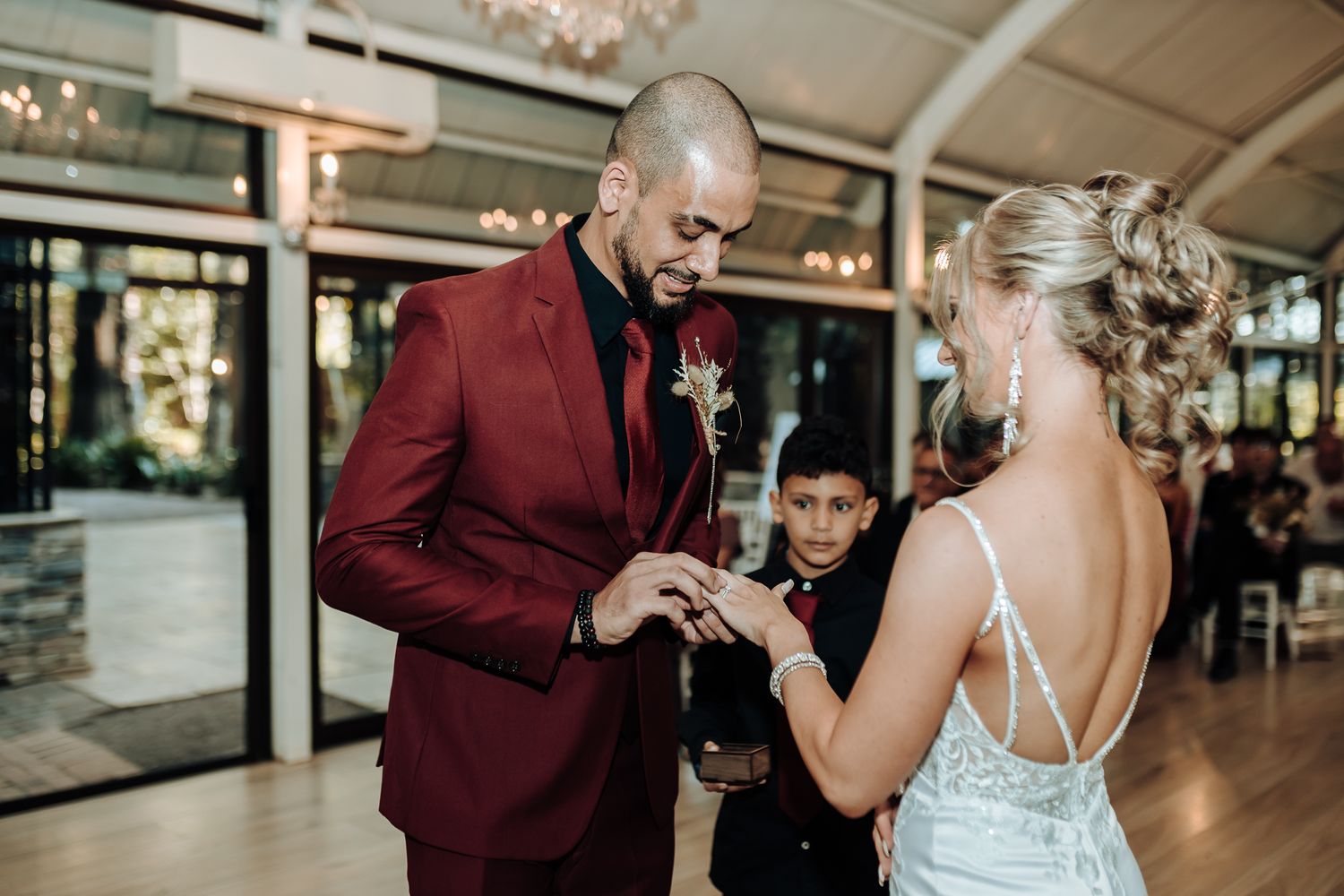 Wedding ring exchange ceremony in an elegant venue with crystal chandeliers.