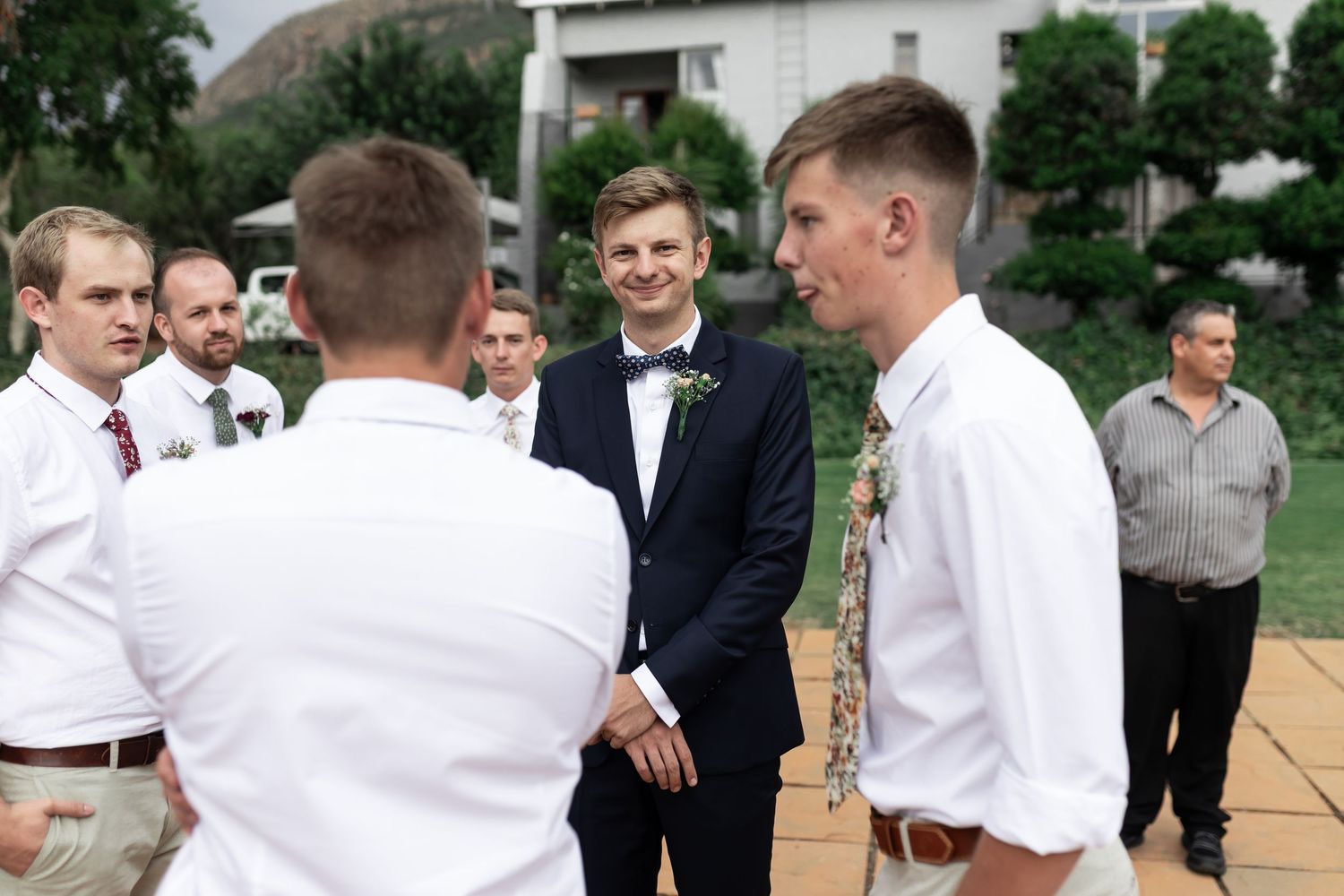 Groomsmen sharing a lighthearted moment before the wedding ceremony on an outdoor patio.
